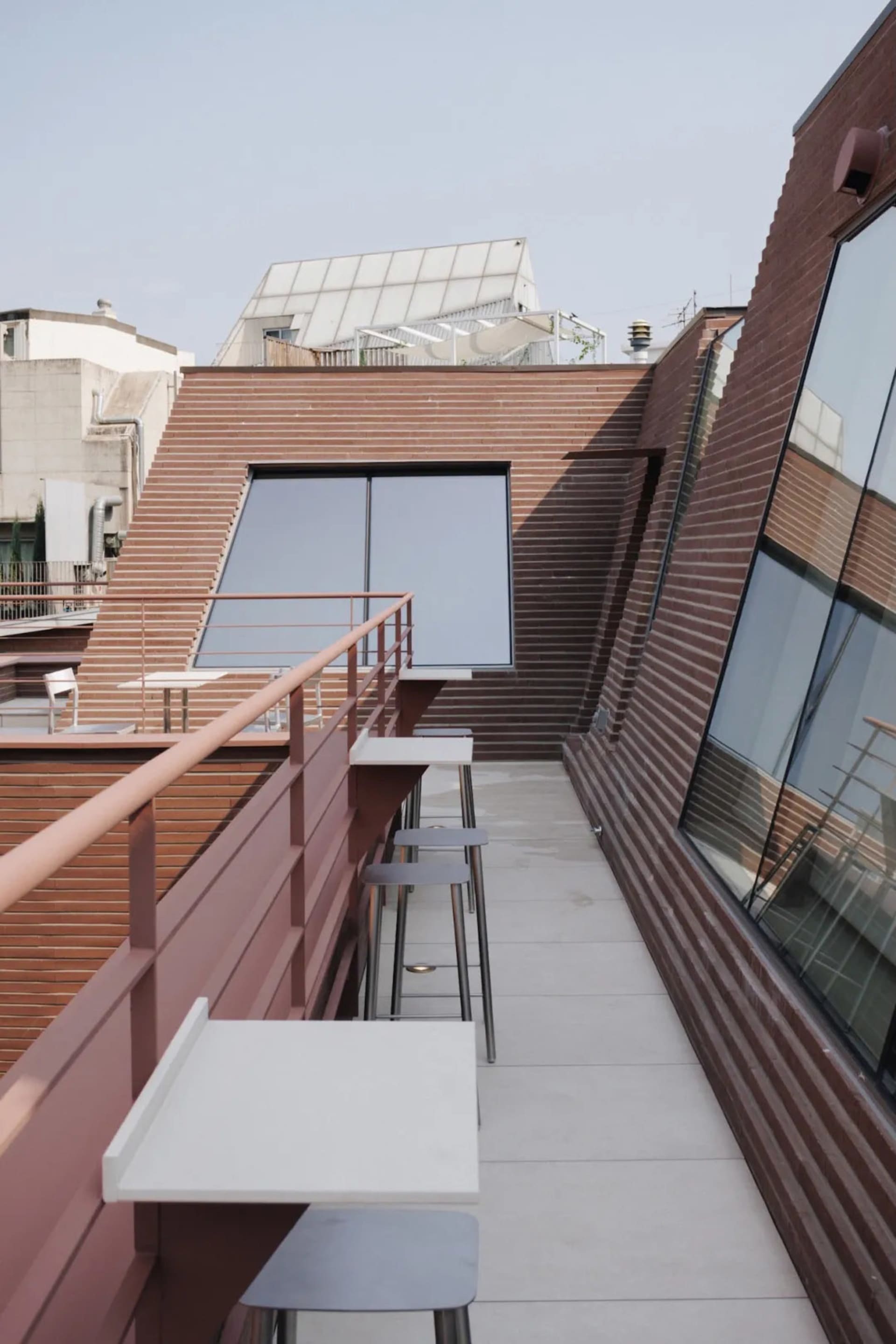 Photograph of a modern building with a brick facade, large window, and balcony, featuring a comfortable and inviting interior with chairs and dining tables