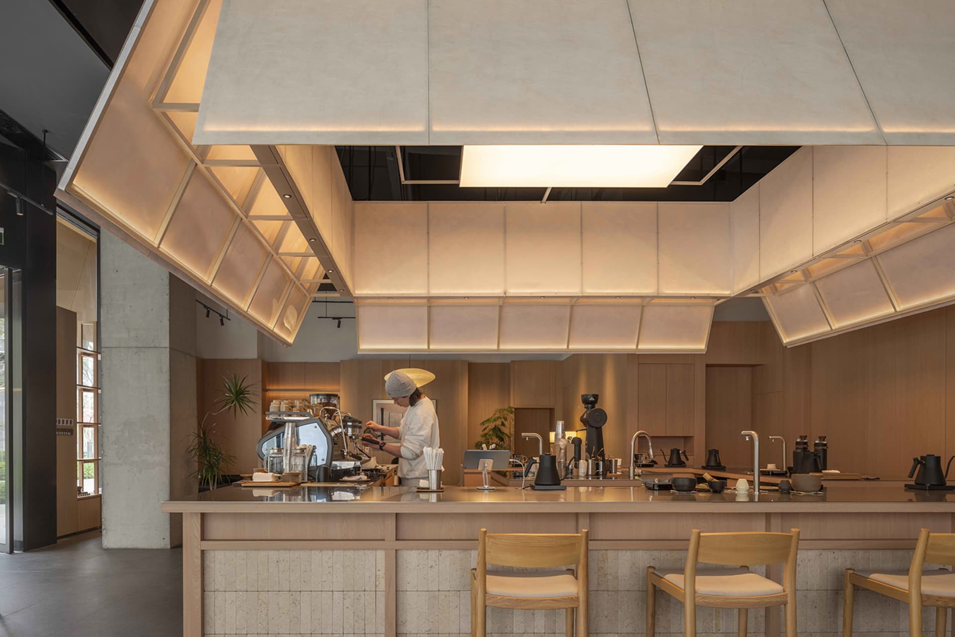 Dimly lit kitchen with a wooden counter, chairs, and dining table, featuring a coffee maker and a cup on the counter