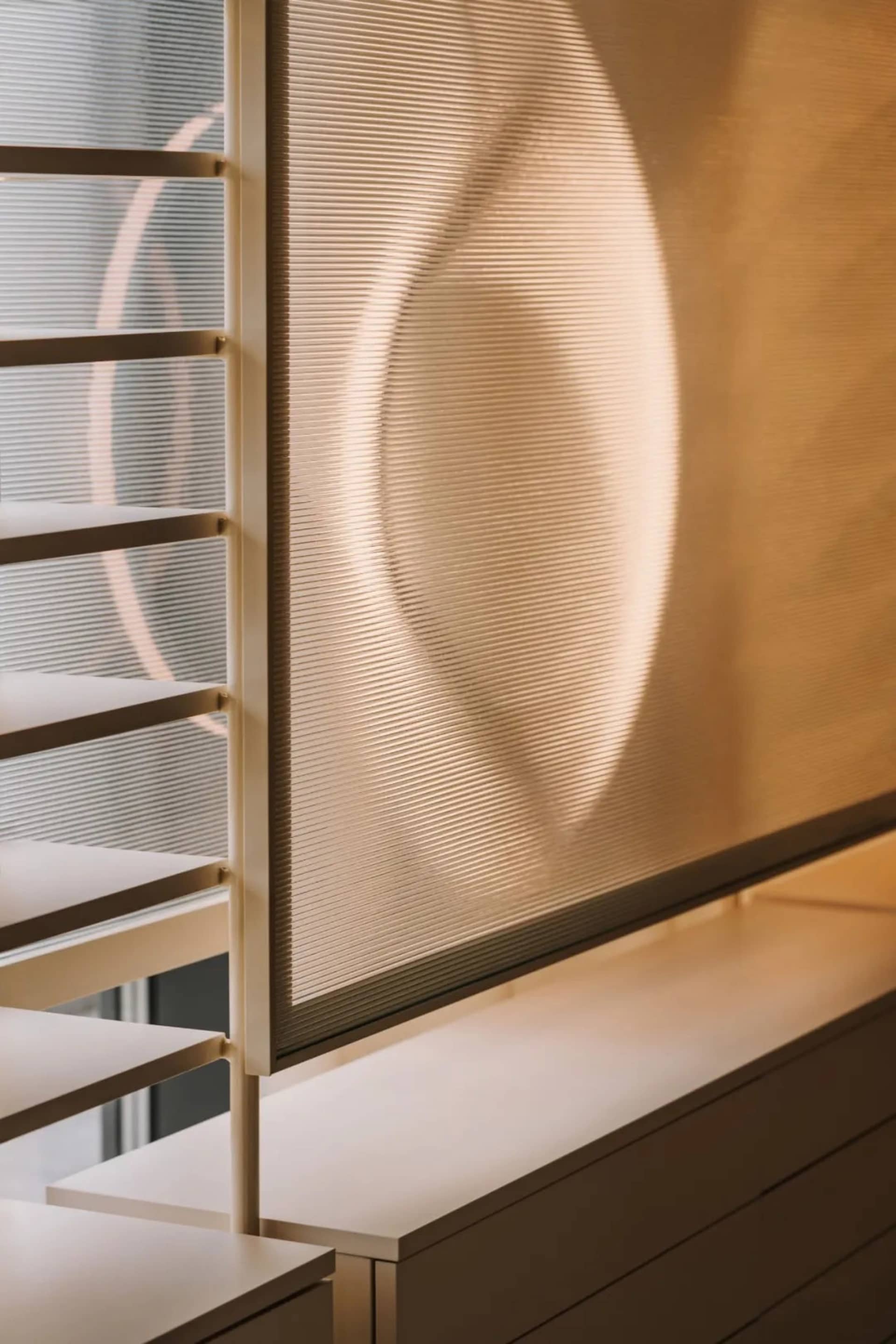 A room with a white wall and a window with a mesh shade drawn down, allowing natural light to filter in