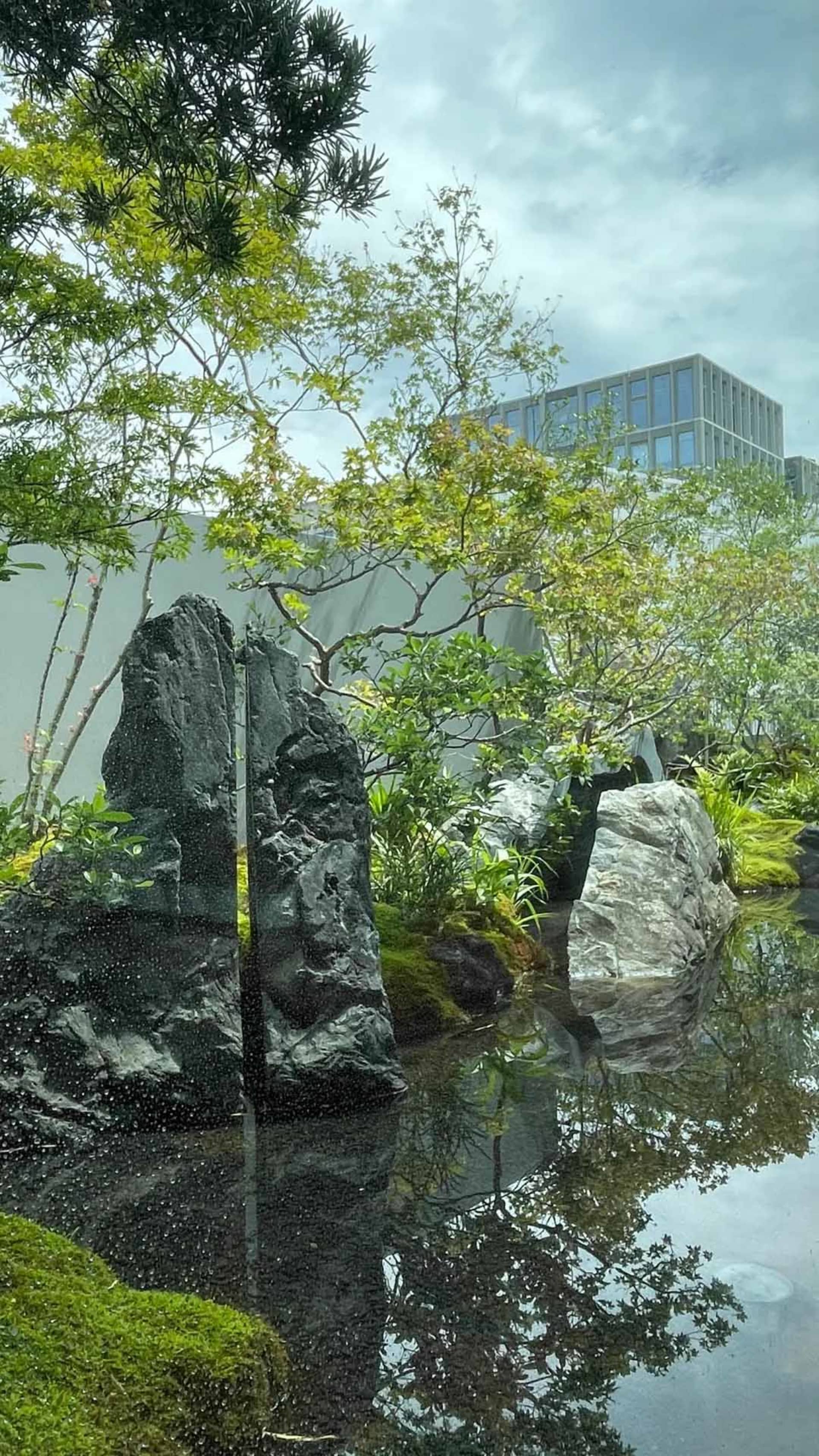 一處謙靜的戶外空間，現代建築、巨大的窗戶和反射池，週圍是自然和人工元素