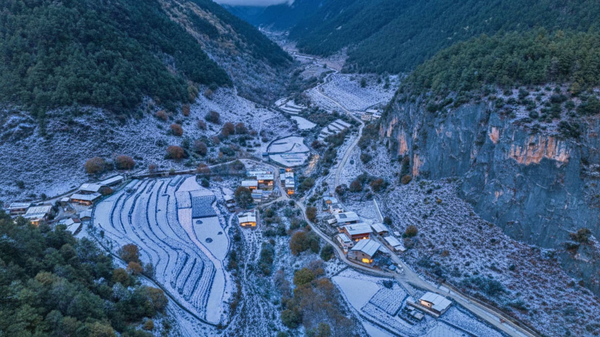 A snow-covered village set against a mountain backdrop, featuring traditional houses and buildings with snow-covered roofs and windows