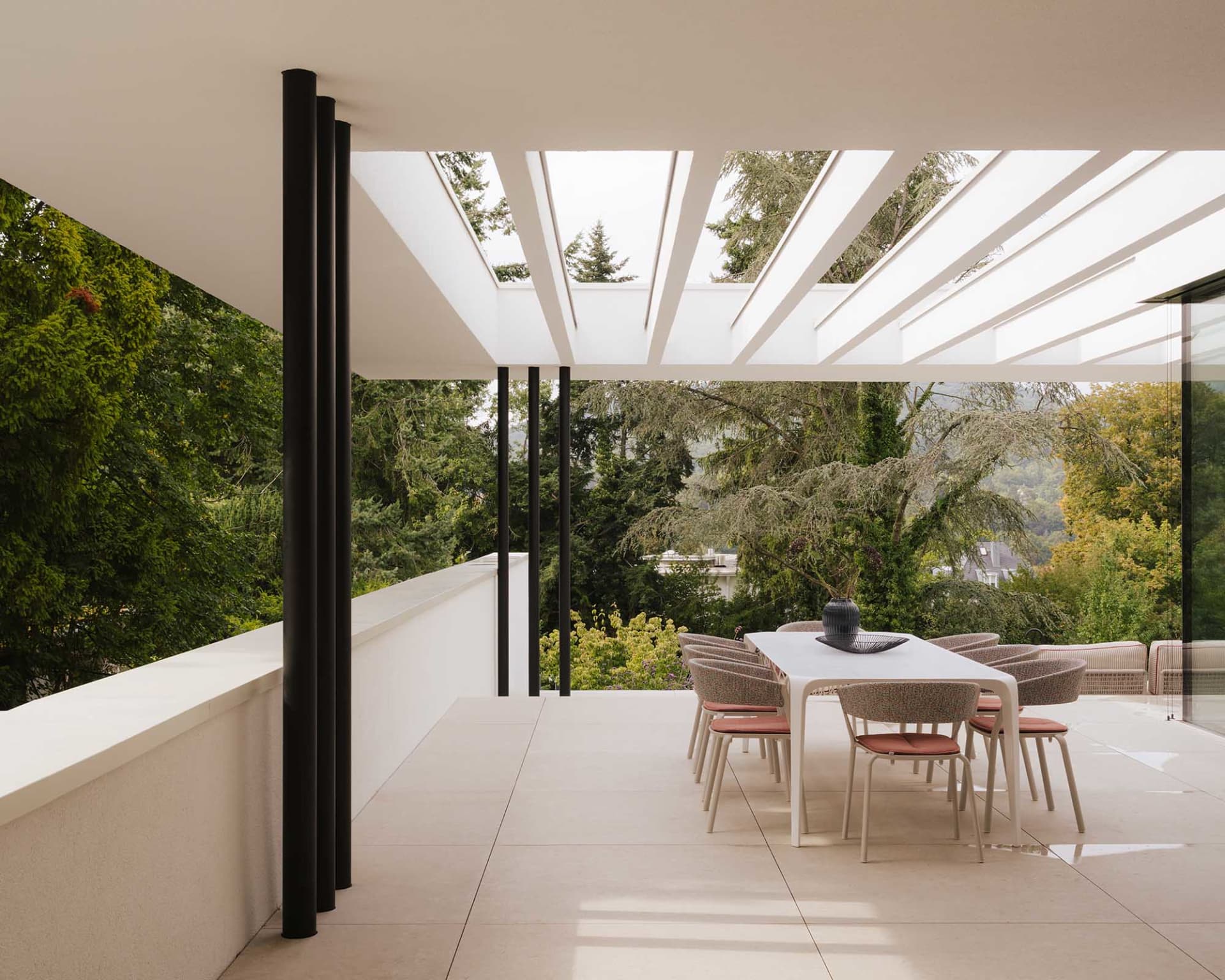 A well-lit outdoor patio with a white dining table surrounded by red chairs, set in a garden with a view of the mountains in the background