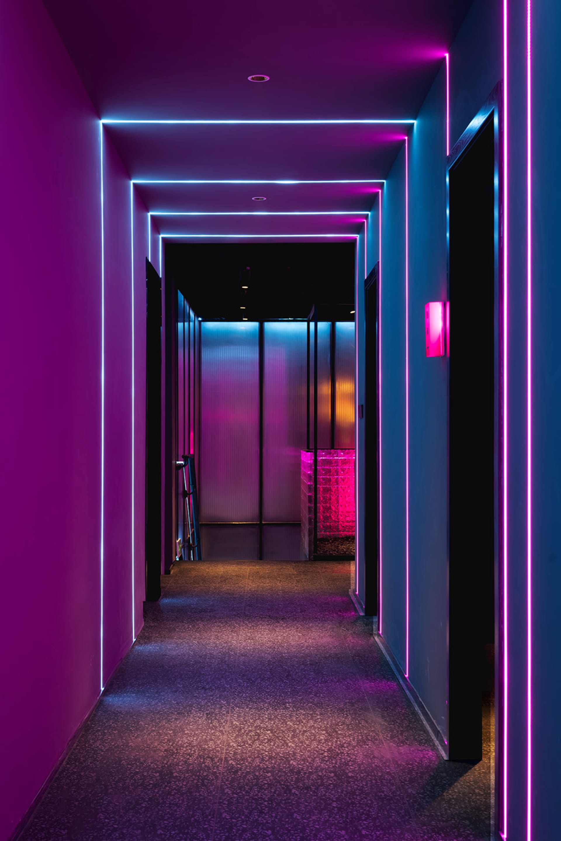 A modern hallway with pink carpet and glass walls, lit by purple lighting, creating a striking contrast and unique atmosphere