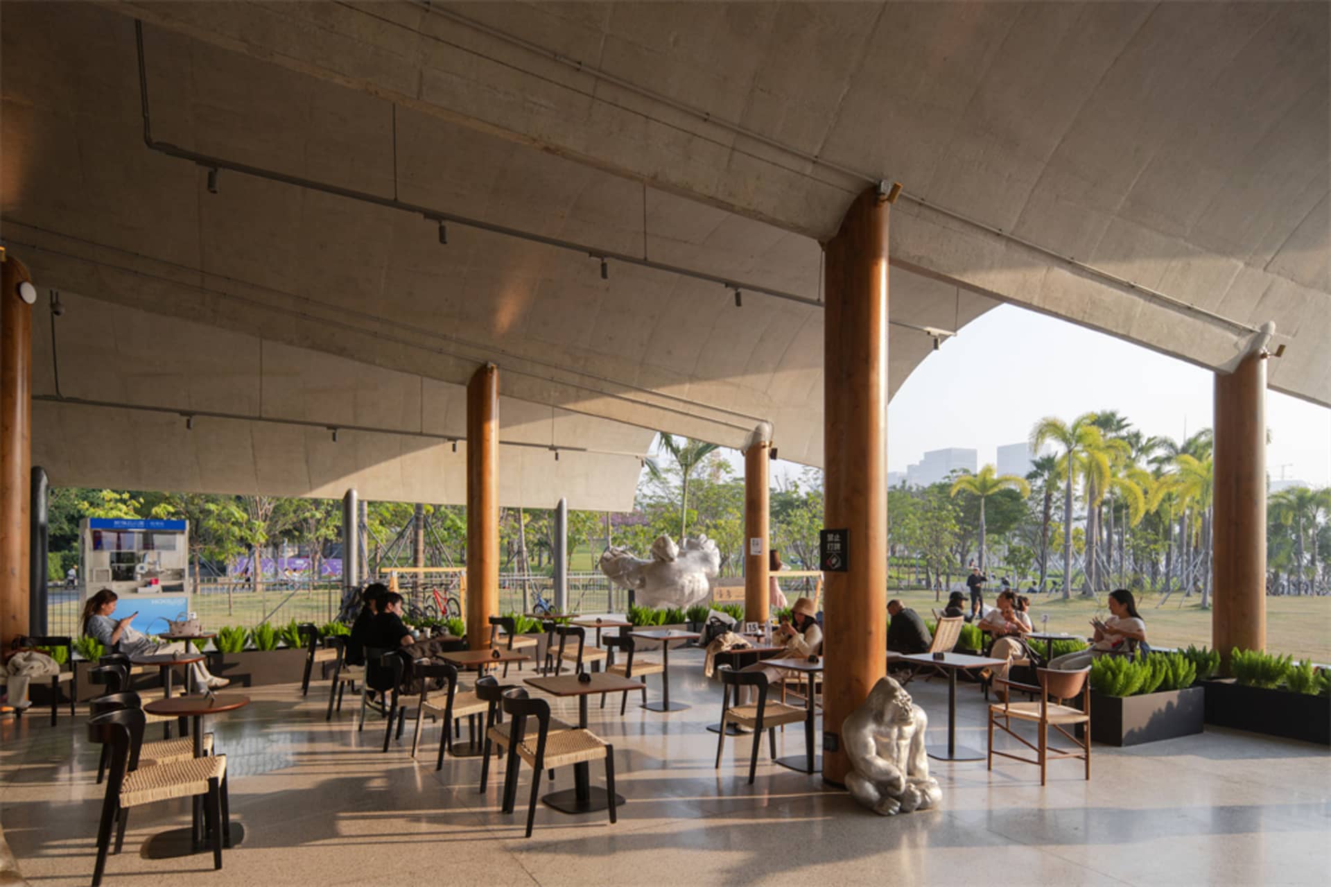 A large open space with a high ceiling, featuring various furniture, people, and natural light from windows, with a modern and stylish atmosphere