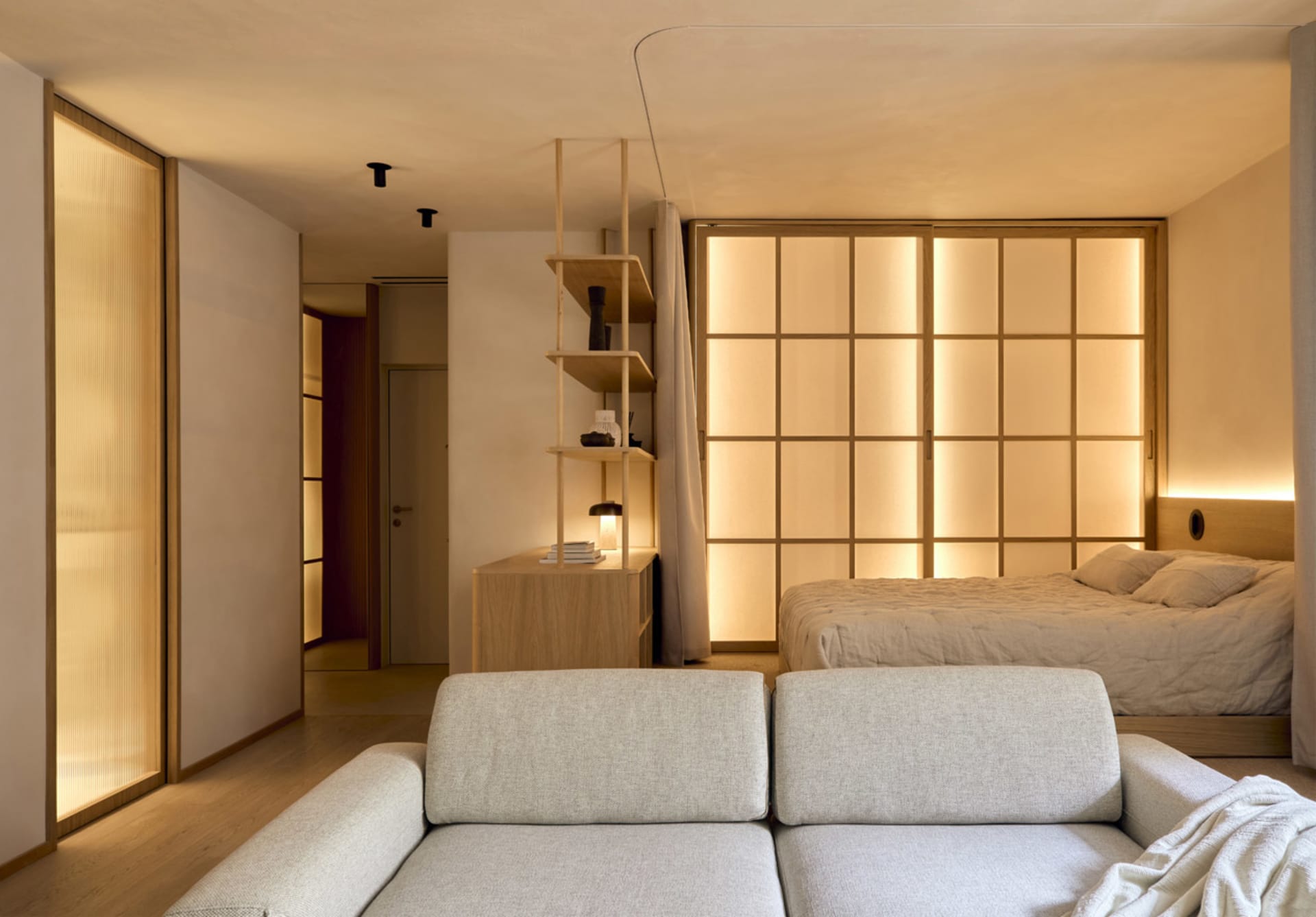 Cozy bedroom with a bed, couch, and bookshelf, set against a white wall and wooden floor, with dim lighting