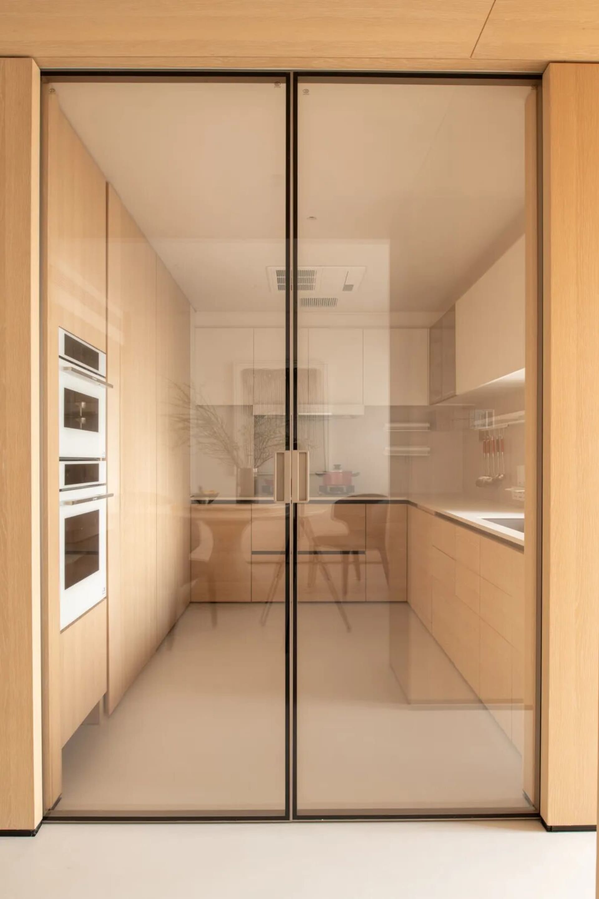 Modern kitchen with wooden cabinets, glass door, and appliances, featuring a refrigerator, oven, and sink, with natural light entering through the open door