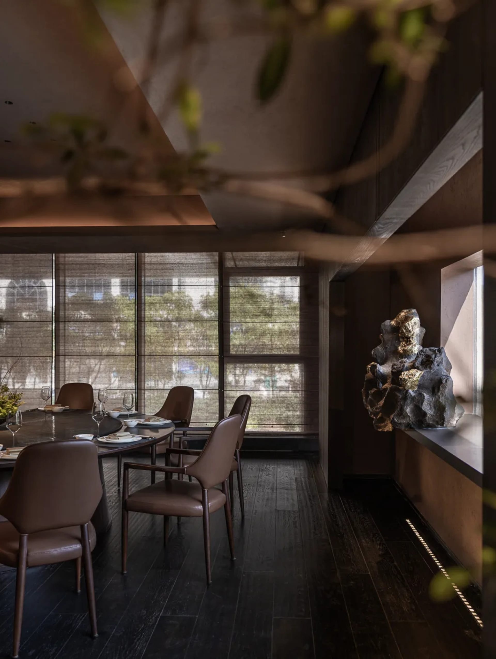 Dining room with a large window, modern dining table, chairs, wine glasses, potted plant, and vase, lit by natural light