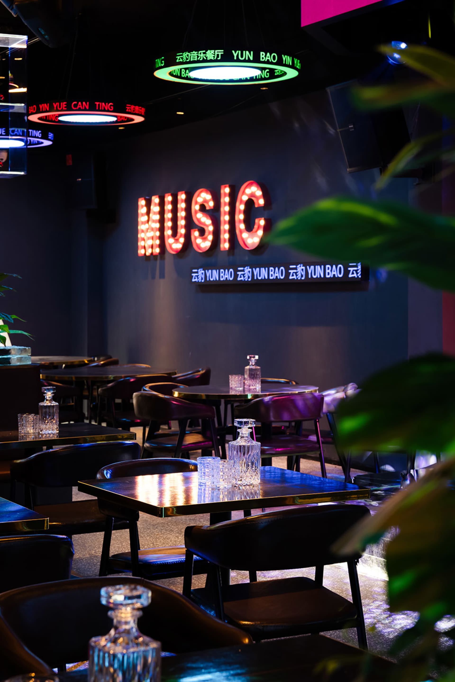 A modern restaurant with a black and white color scheme, featuring a dining area with tables and chairs, a bar, and dim lighting creating a cozy atmosphere