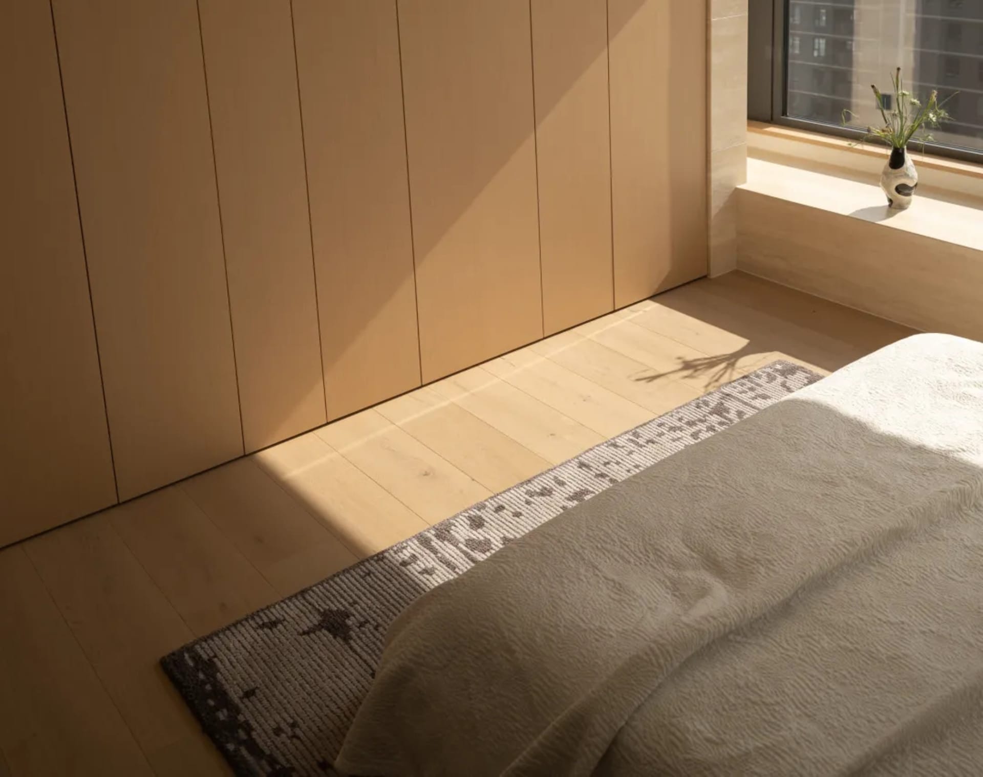 Cozy bedroom with a bed on a wooden floor, a wooden door, and a window in the background, well-lit and inviting