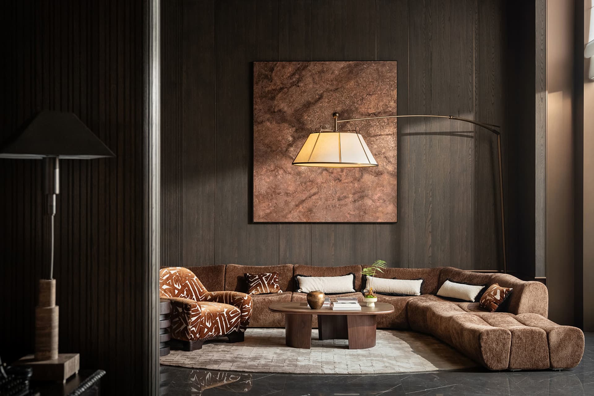 Cozy living room with a brown couch, a chair, and a coffee table, featuring a large painting on the wall and decorative items, with dim lighting creating a warm ambiance