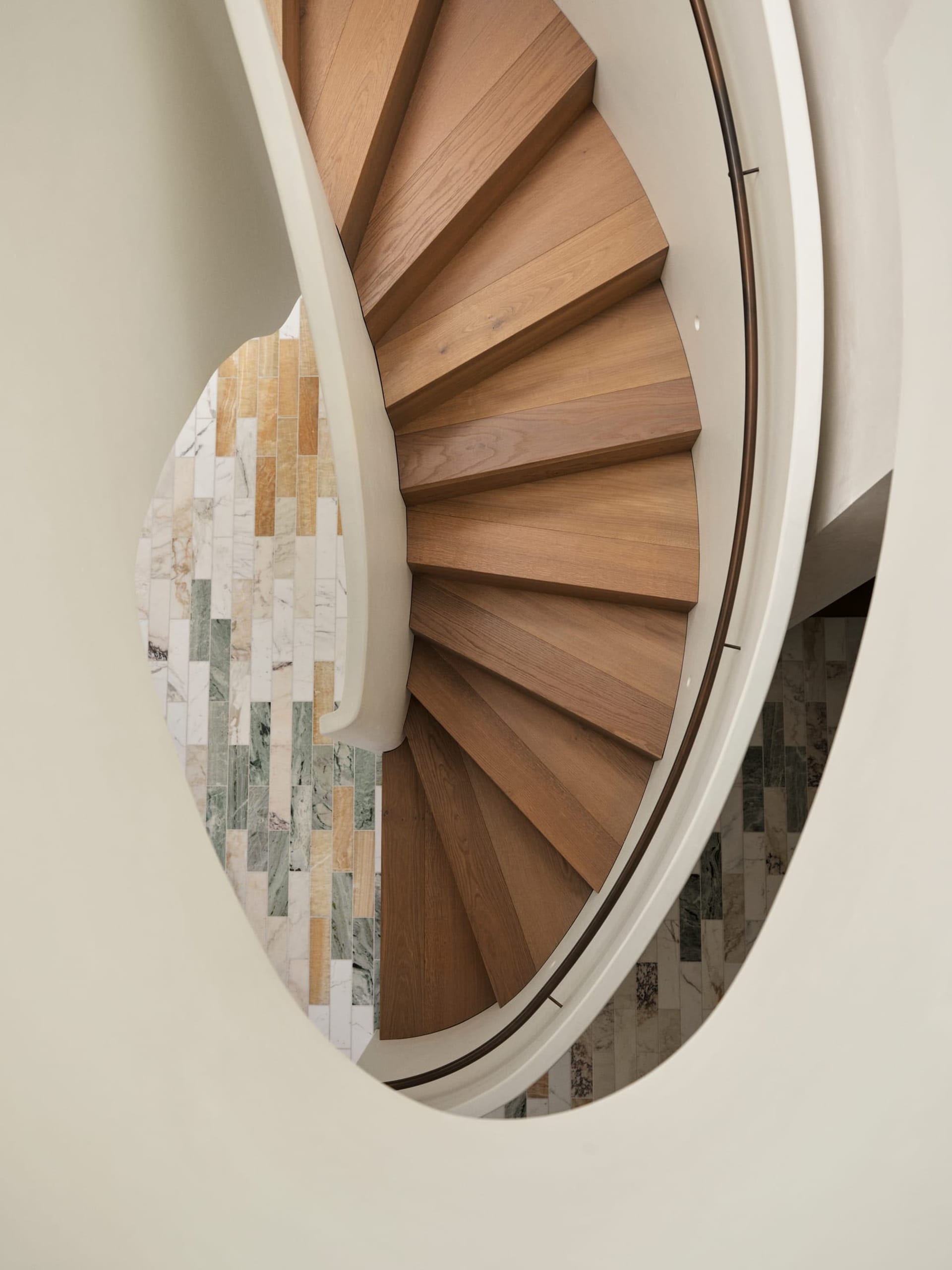 A spiral staircase in a room with a white color scheme, surrounded by natural light and elegant architecture