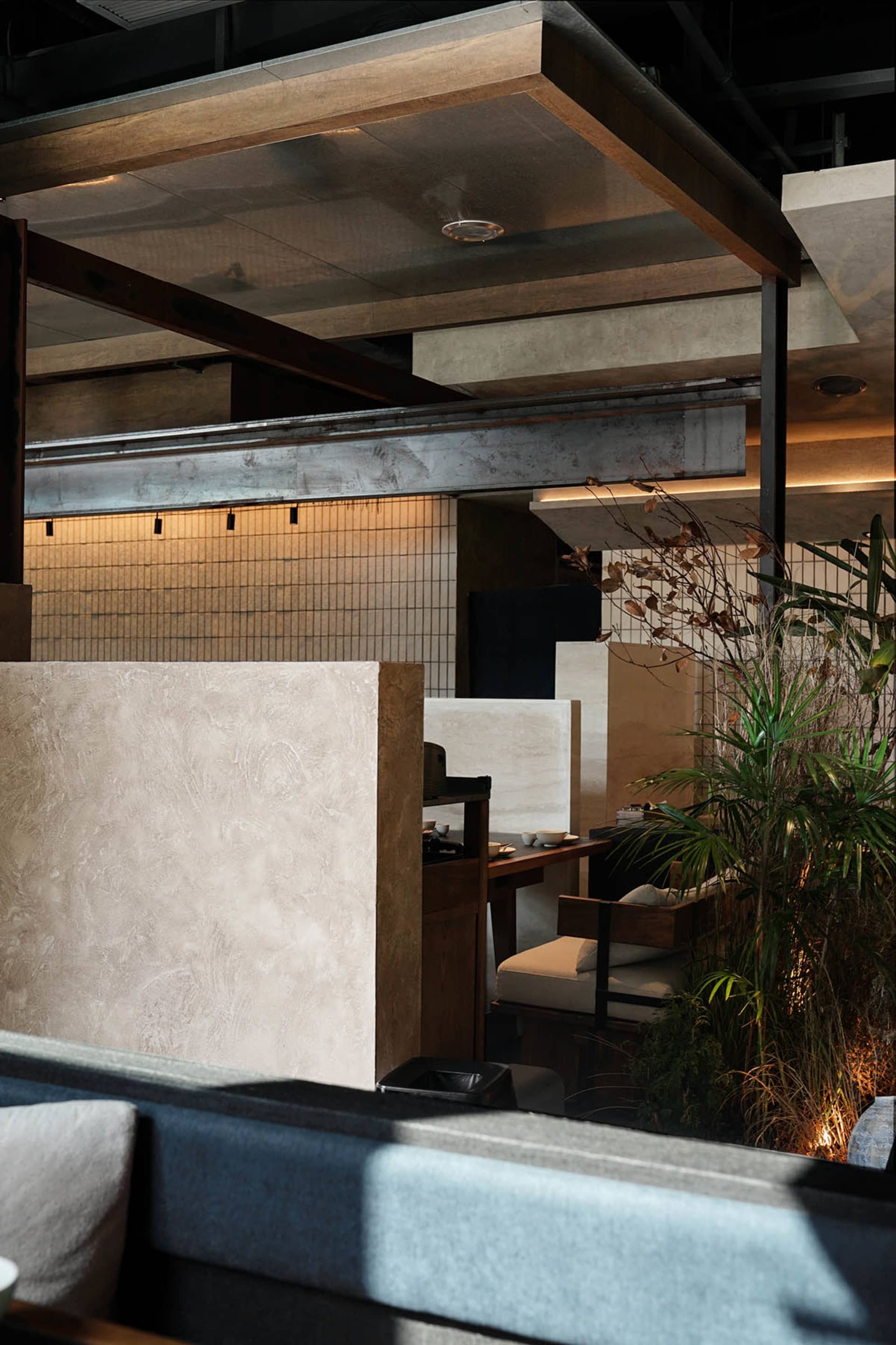 A modern restaurant space with a wooden floor, stone wall, and comfortable seating areas with dining tables and chairs, well-lit with natural light and a potted plant