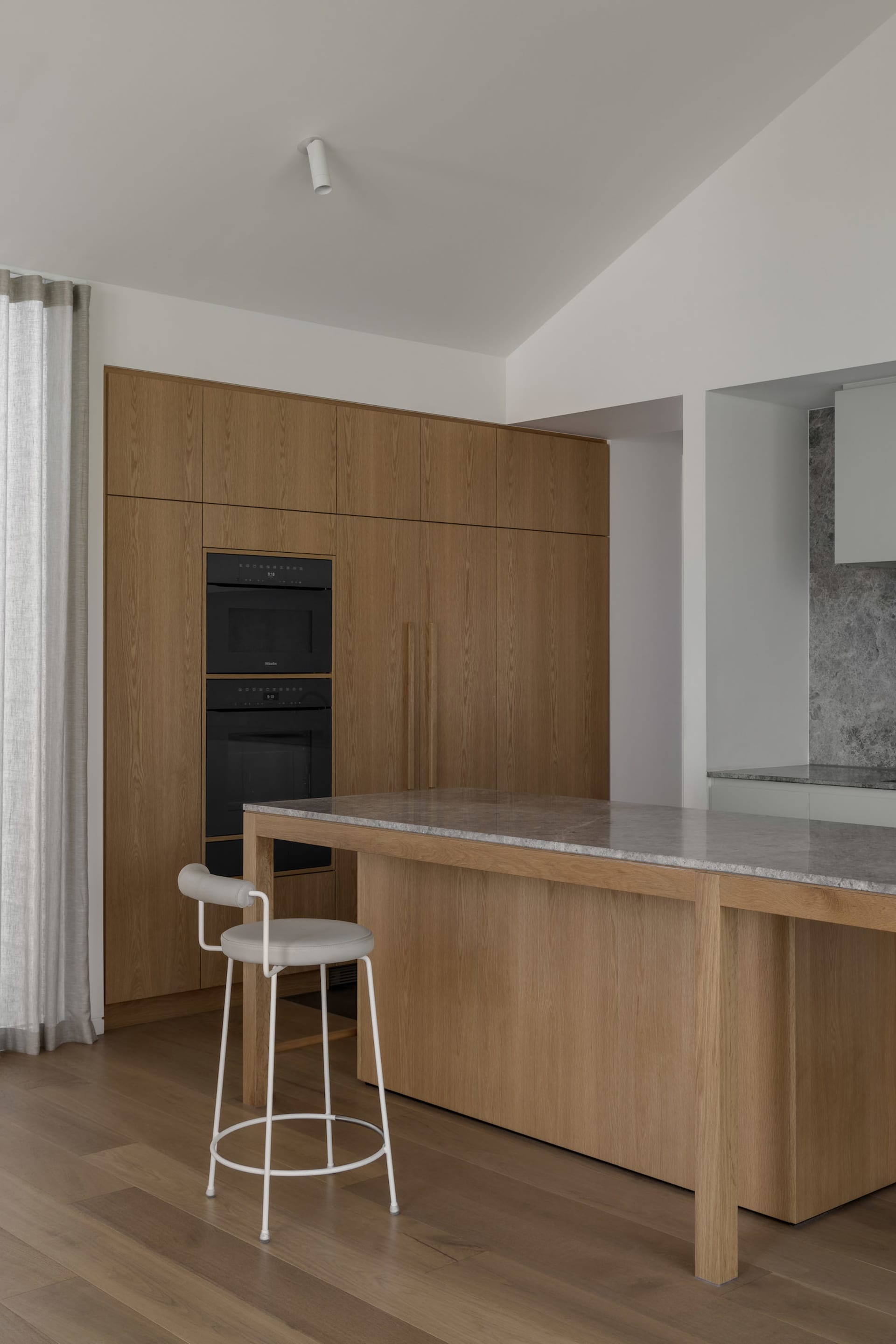 Modern kitchen with wooden cabinets, marble countertop, black oven, sink, refrigerator, chair, and dining table