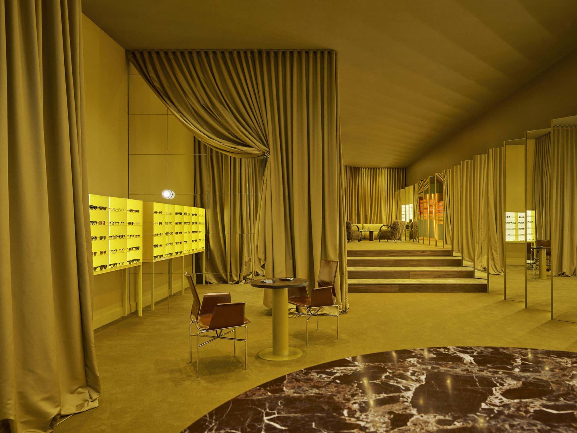 A modern living room with a yellow color scheme, featuring a circular table, couch, and chair, surrounded by yellow curtains, and illuminated by a light source, with a warm and cozy atmosphere created by the lighting and materials