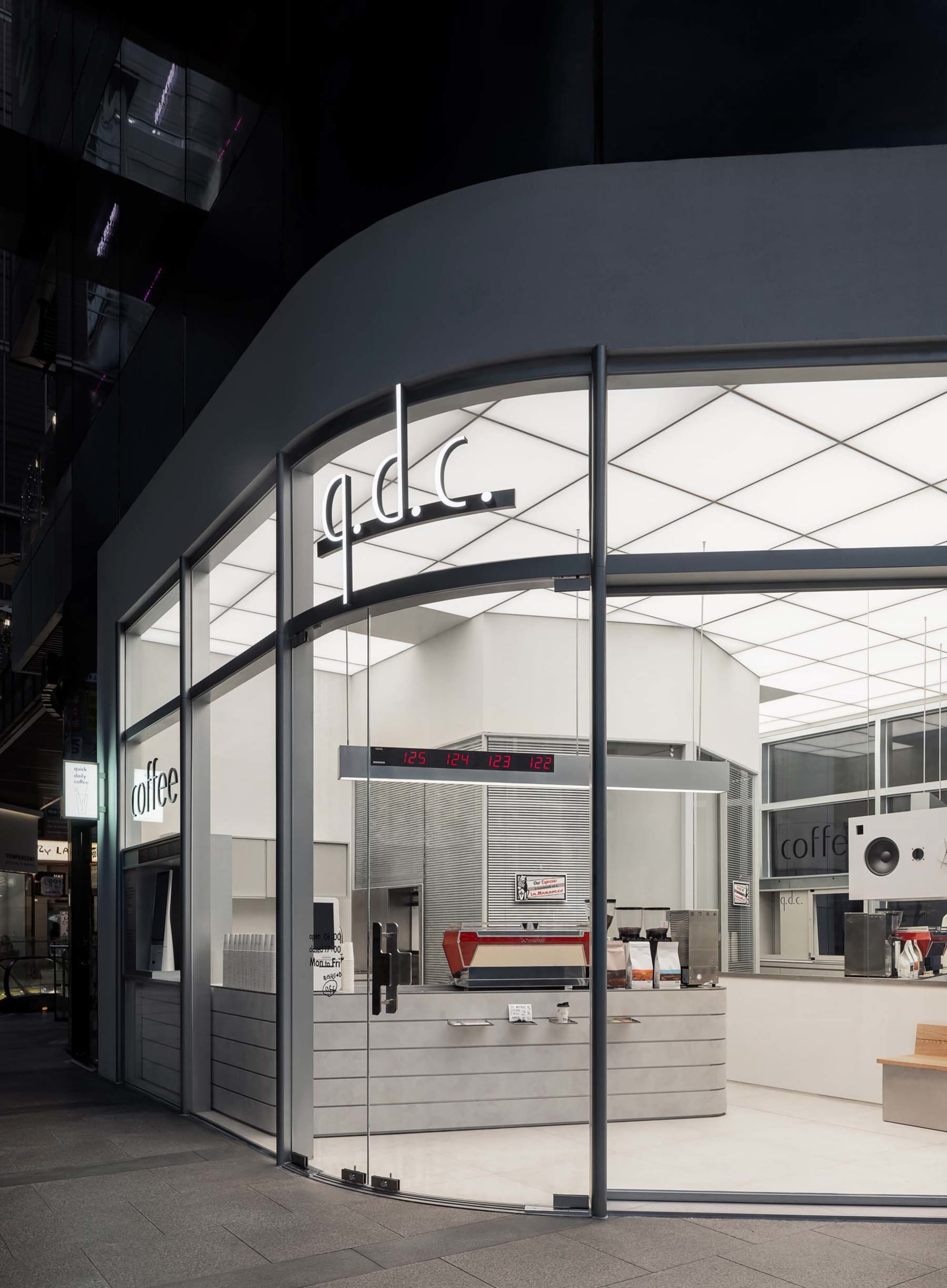 A well-lit coffee shop interior with a modern design, featuring a wooden counter, a coffee machine, and a few cups and a bottle on display