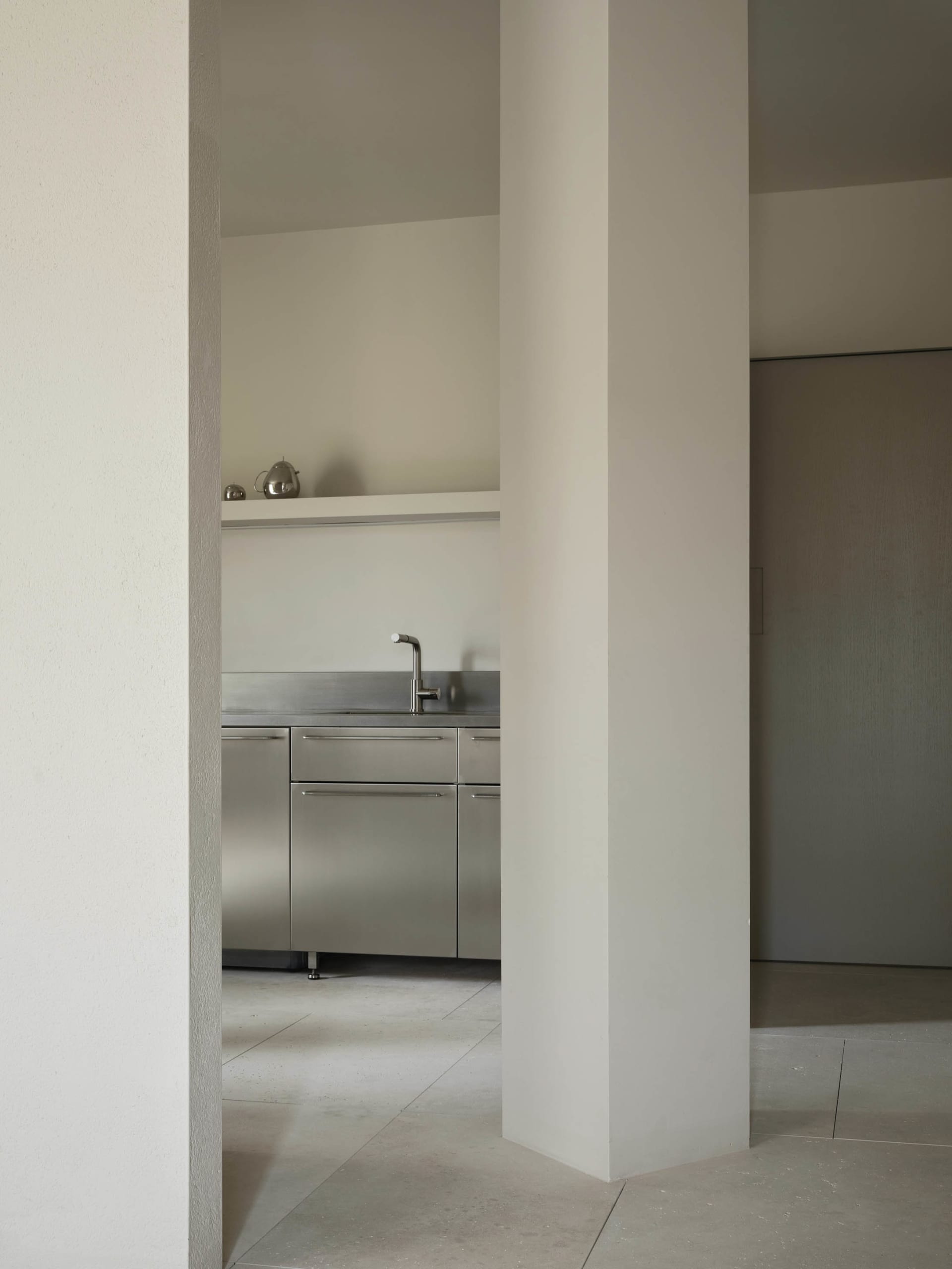 A clean and organized kitchen with a white color scheme, a stainless steel sink, and a refrigerator on the left side