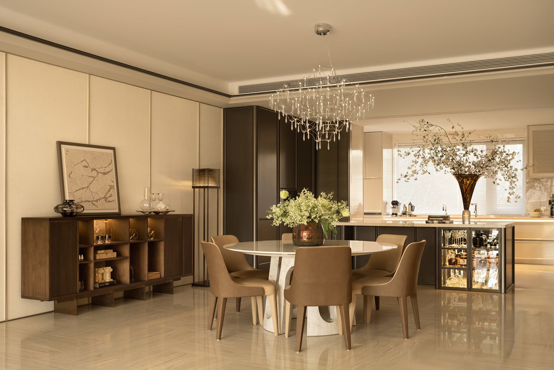 A well-lit and beautifully decorated living room with a dining table, chandelier, wine glasses, and a potted plant, creating an elegant atmosphere