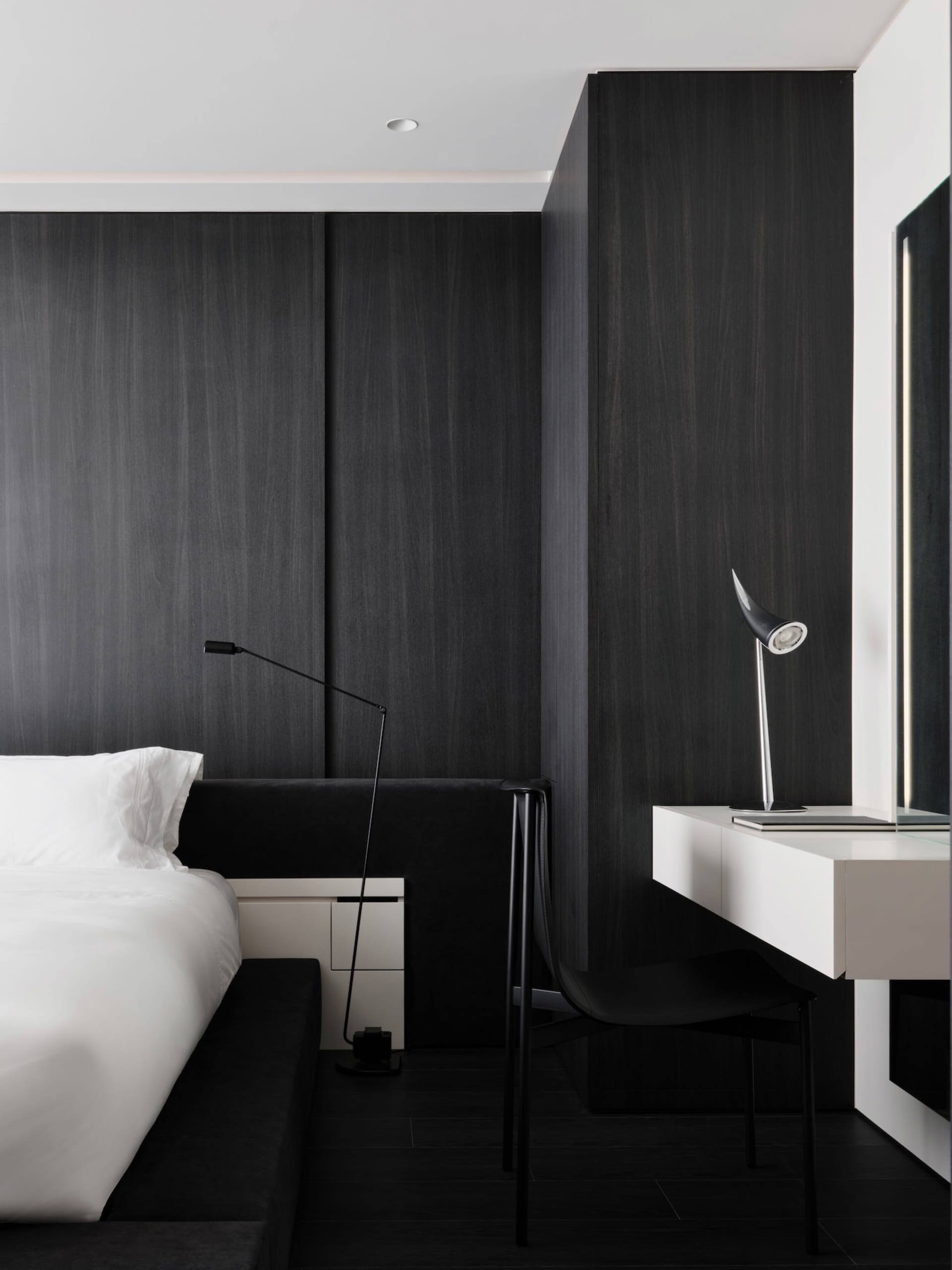 A dimly lit black and white bedroom with a bed, desk, and chair, creating a cozy and intimate atmosphere