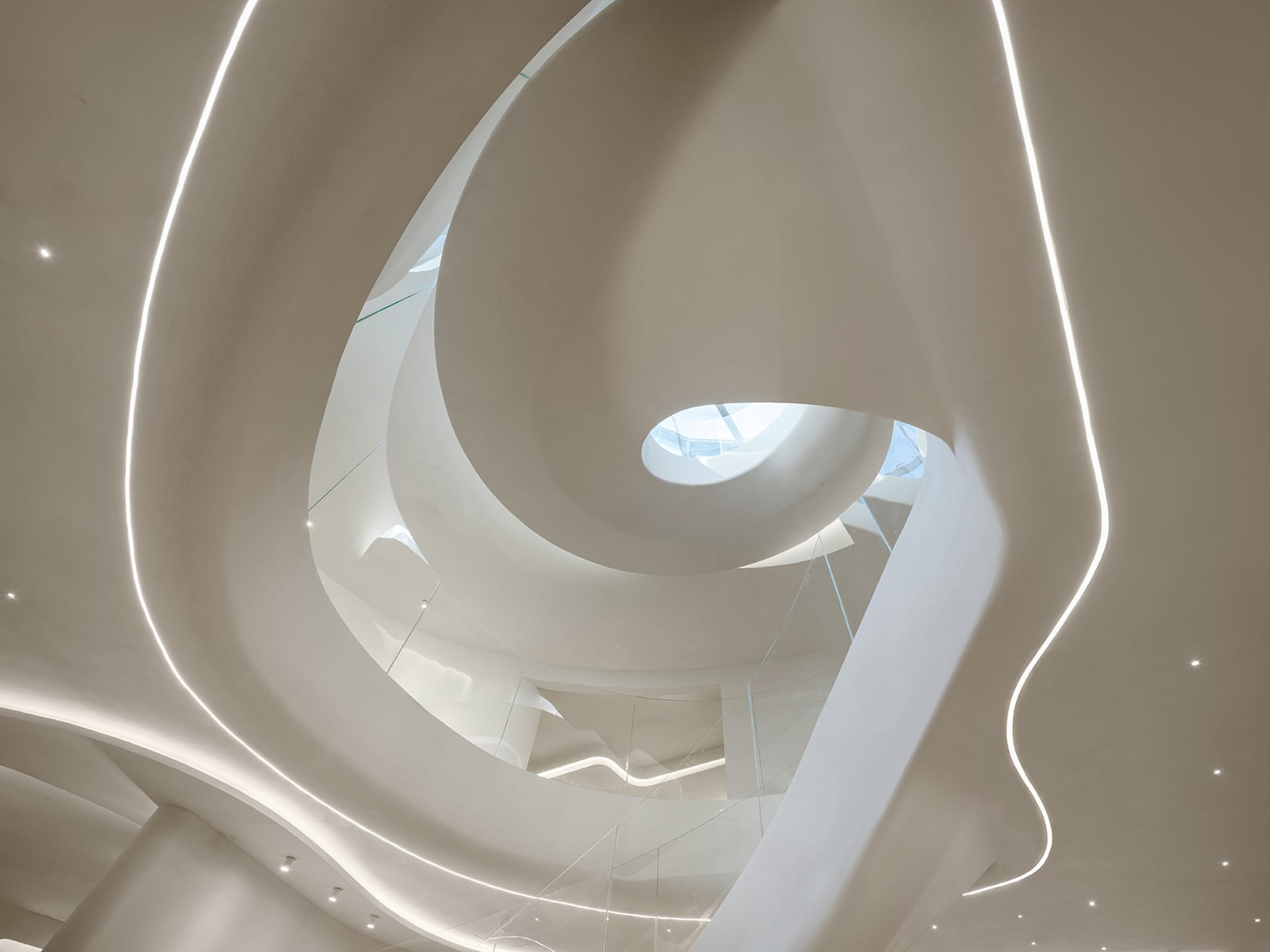 A minimalist museum with a spiral staircase made of concrete and glass railing, bathed in natural light from a window