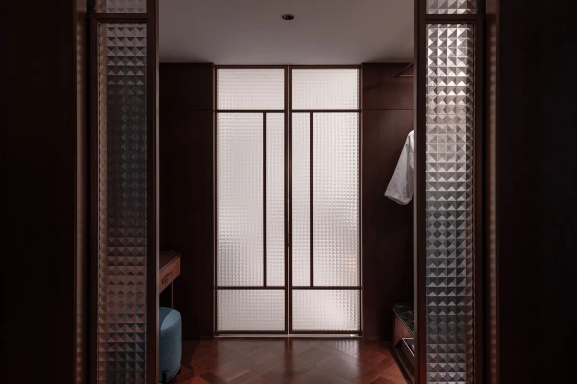 Cozy residential hallway with a wooden floor, glass doors and walls, and dim lighting