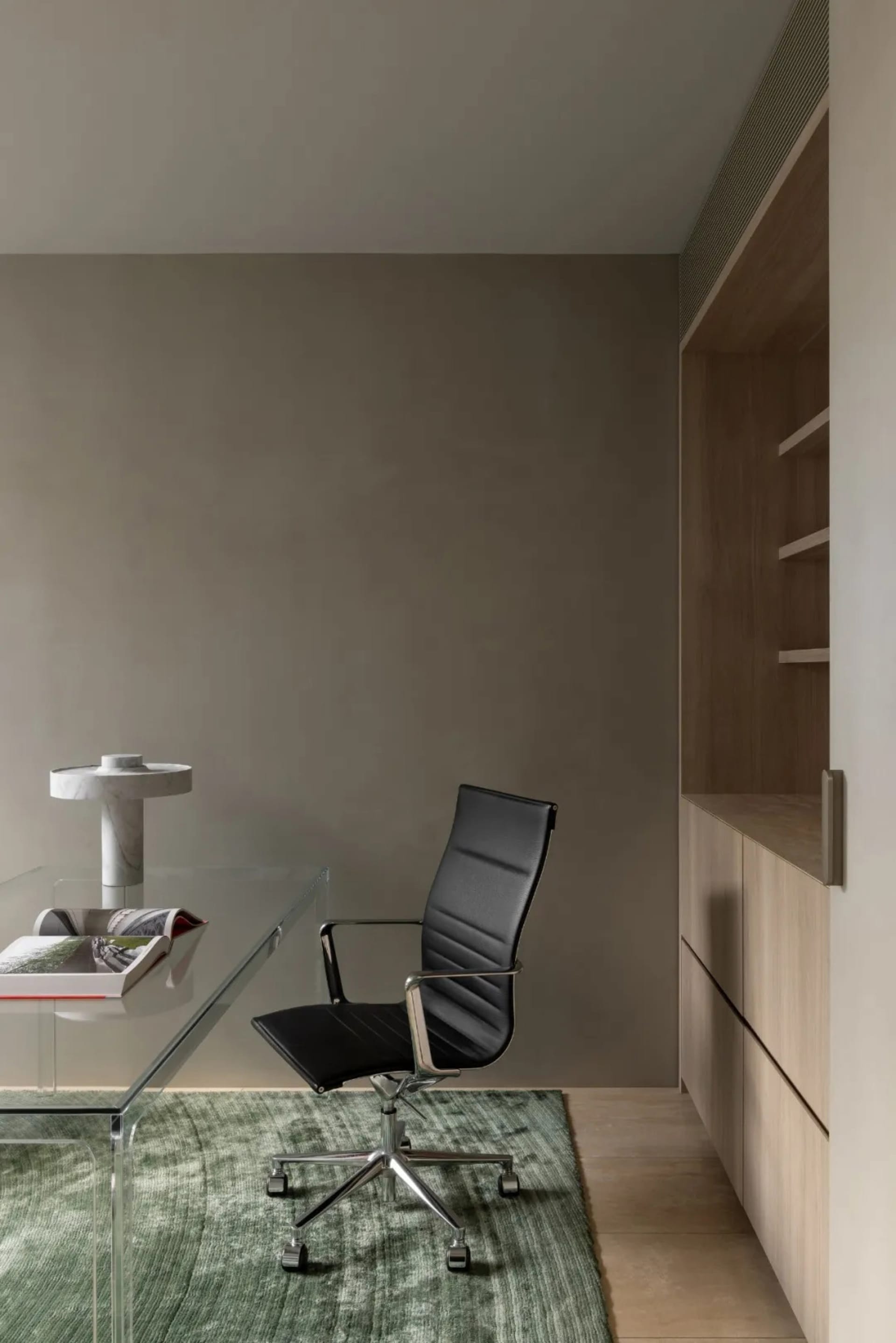 A dimly lit room with a glass table and a black chair, surrounded by a modern and minimalist space with a wall and door in the background