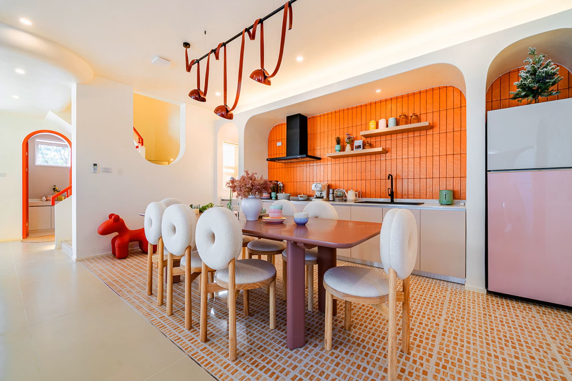 Warm and inviting kitchen with a dining table, wooden chairs, and a vase, surrounded by an orange color scheme and natural light