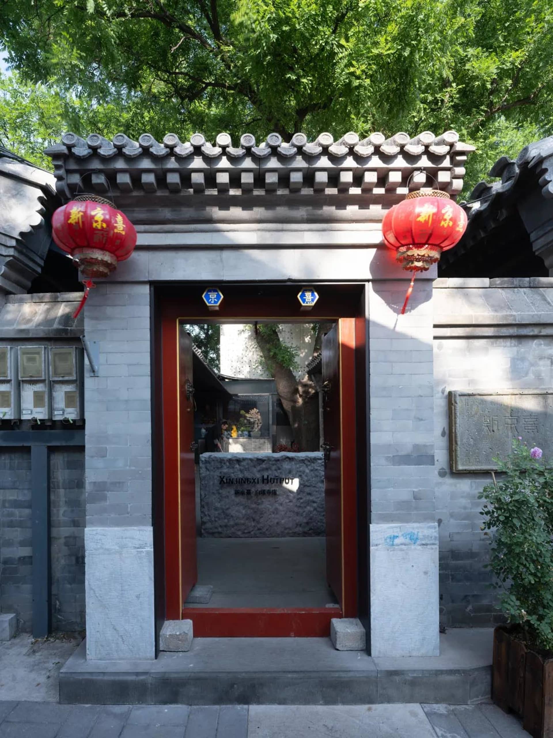 一張中國風格建築的照片，紅色的門和石頭的室內，置於灰色的屋頂和自然景色中，受到暖光的照射