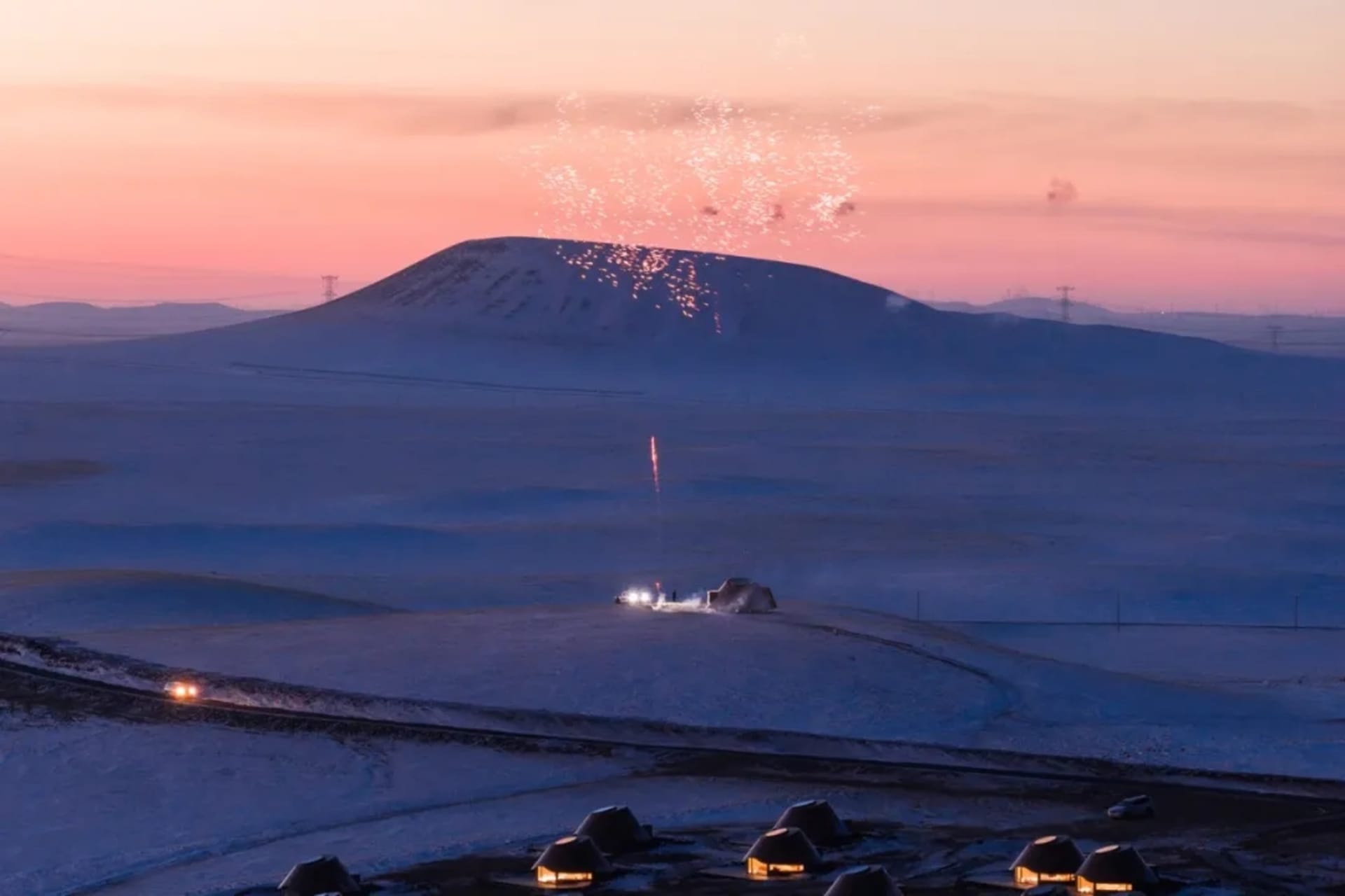 Snowy landscape with a mountain in the background, featuring small wooden cabins and a serene atmosphere