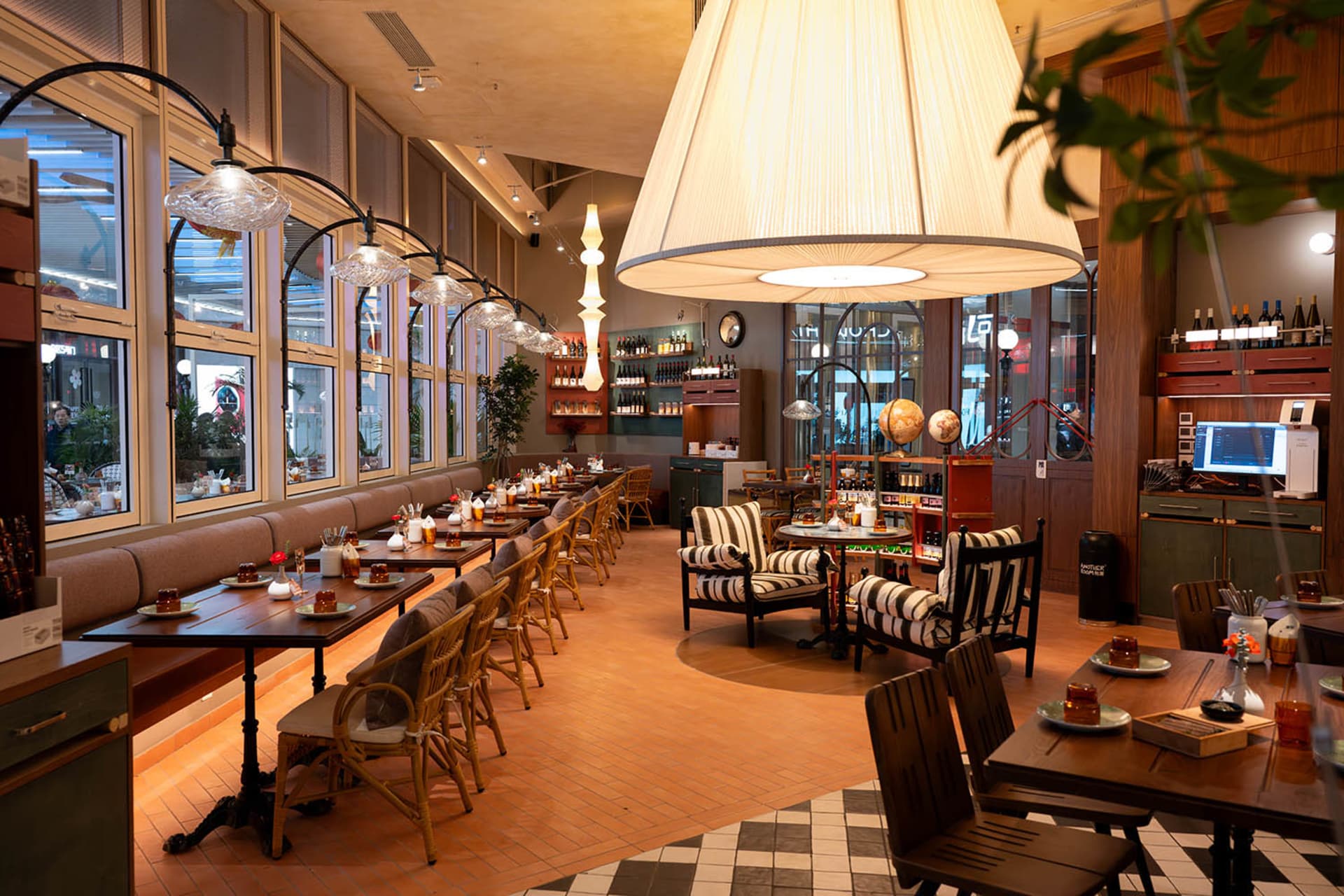 A modern restaurant with a large dining area featuring wooden tables and chairs, potted plants, and a warm and inviting atmosphere