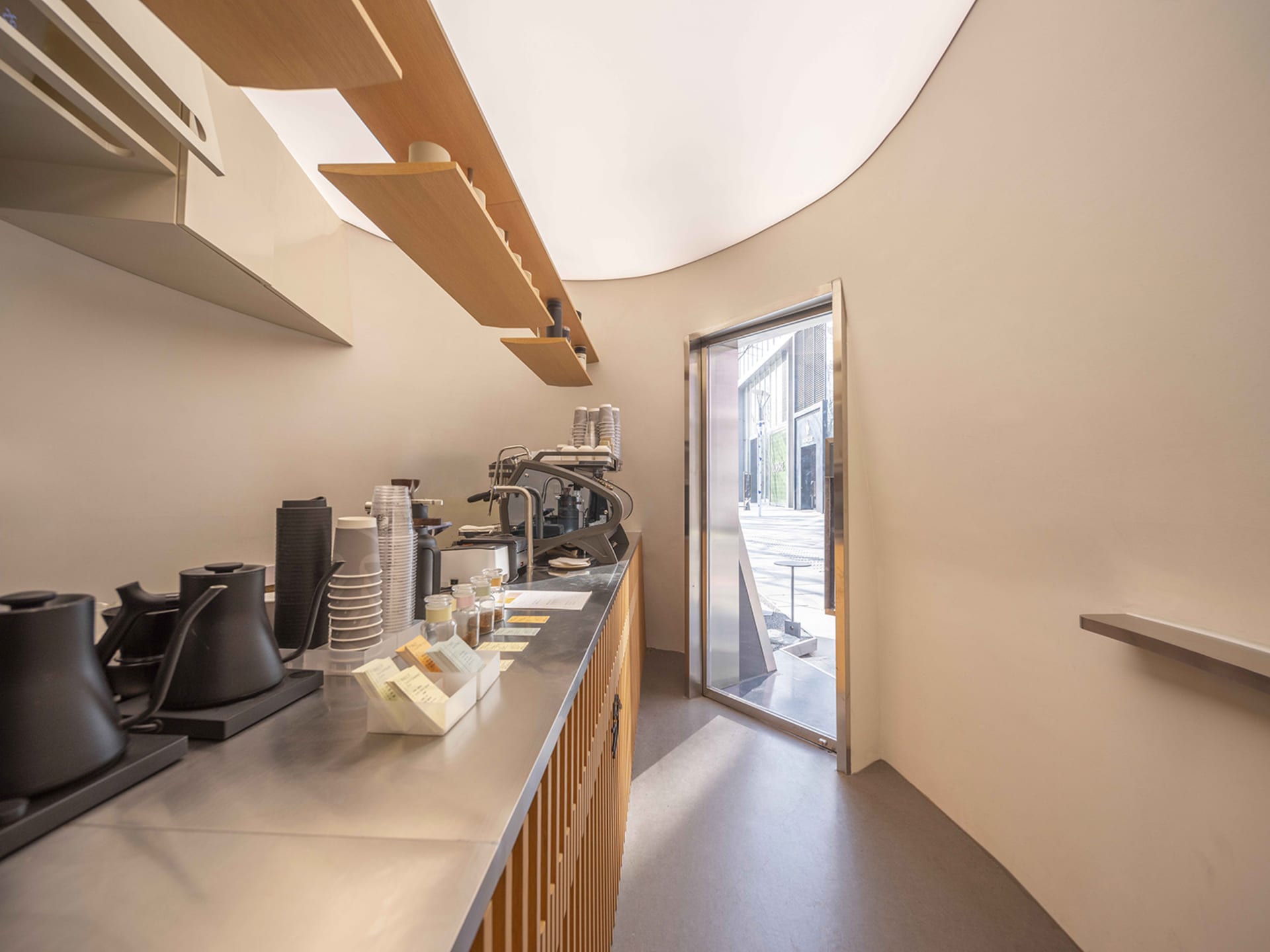 A modern kitchen with a wooden counter, coffee maker, and natural light from the open doorway