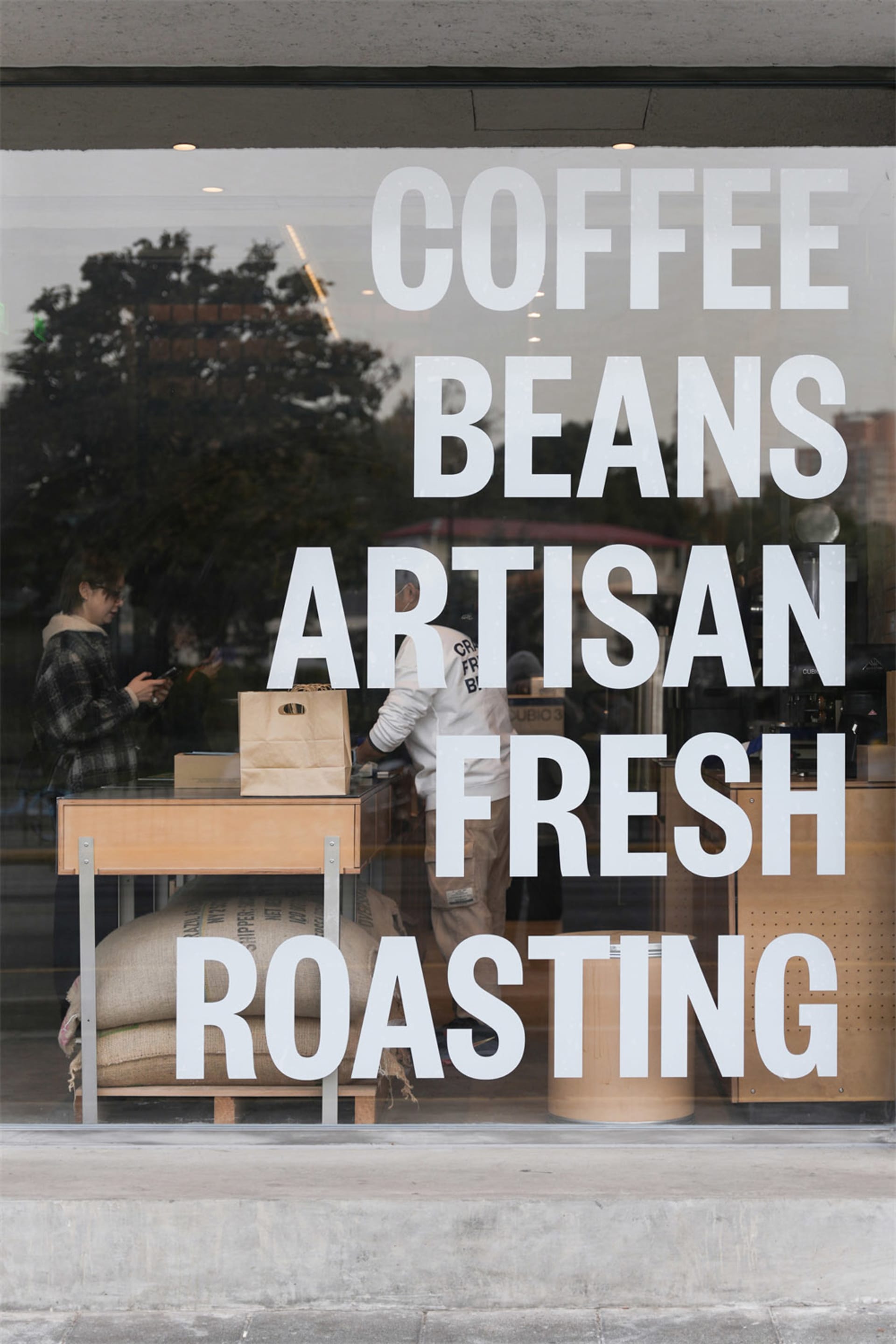 A well-lit coffee shop with a cozy atmosphere, wooden accents, and a window display showcasing freshly roasted coffee beans and the roasting process