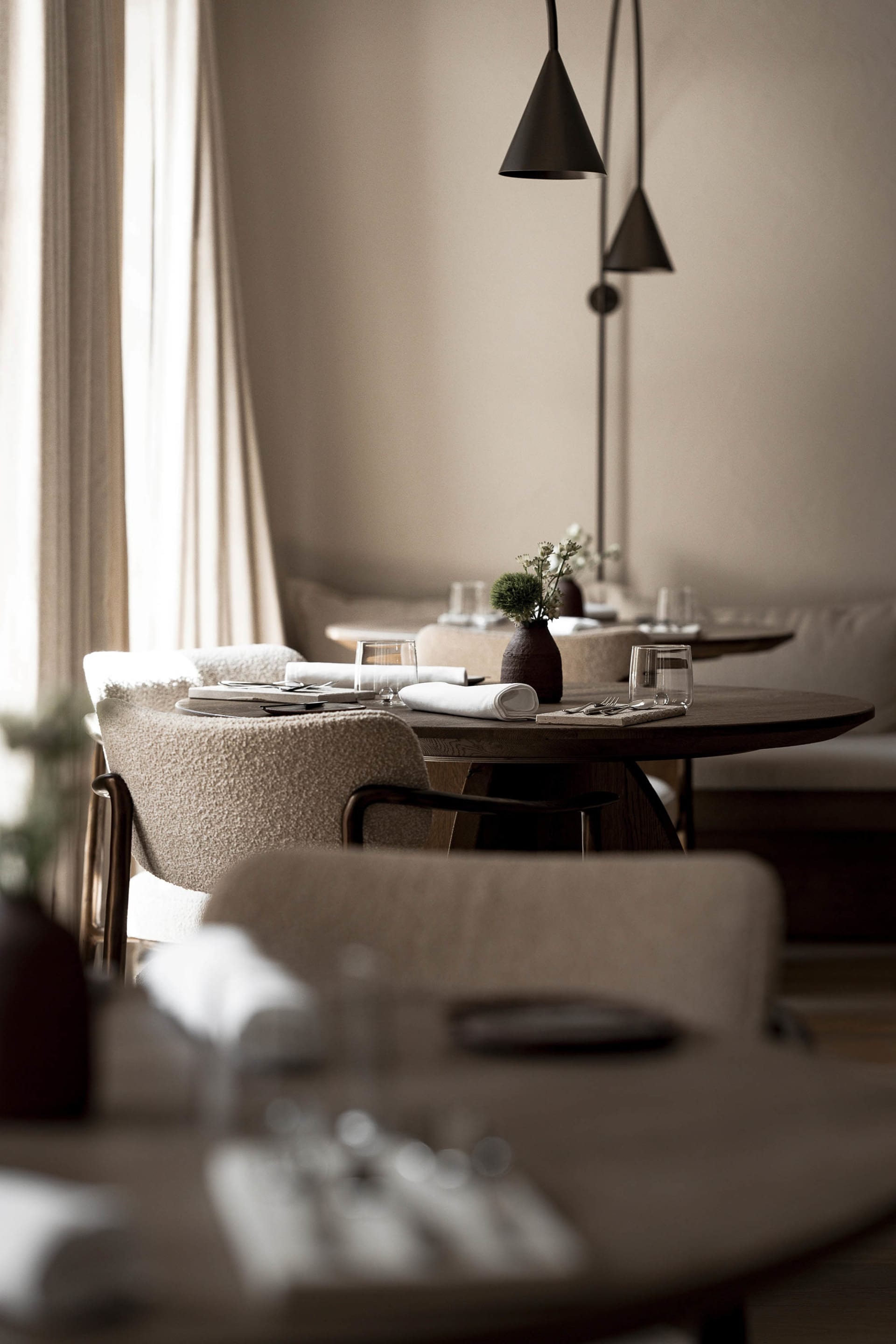 A modern restaurant dining area with white tablecloths, potted plants, and elegant decor, featuring a warm and inviting atmosphere