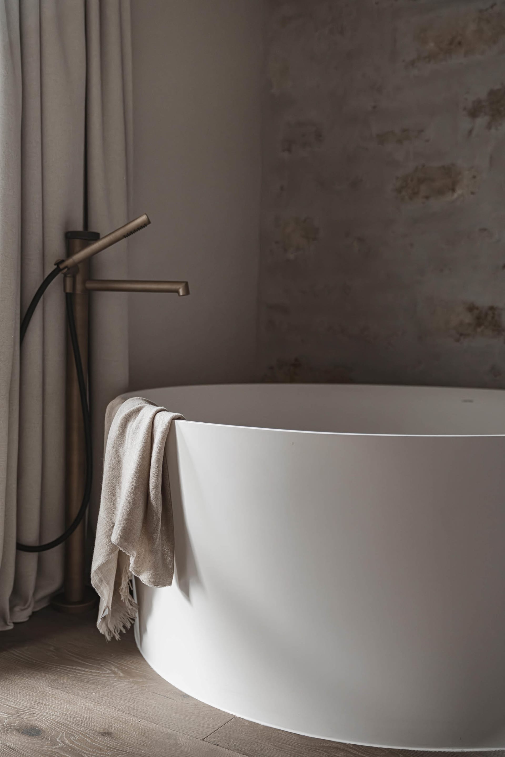 Dimly lit bathroom with a white bathtub under a window, a wool towel hanging on the side, and a cozy atmosphere