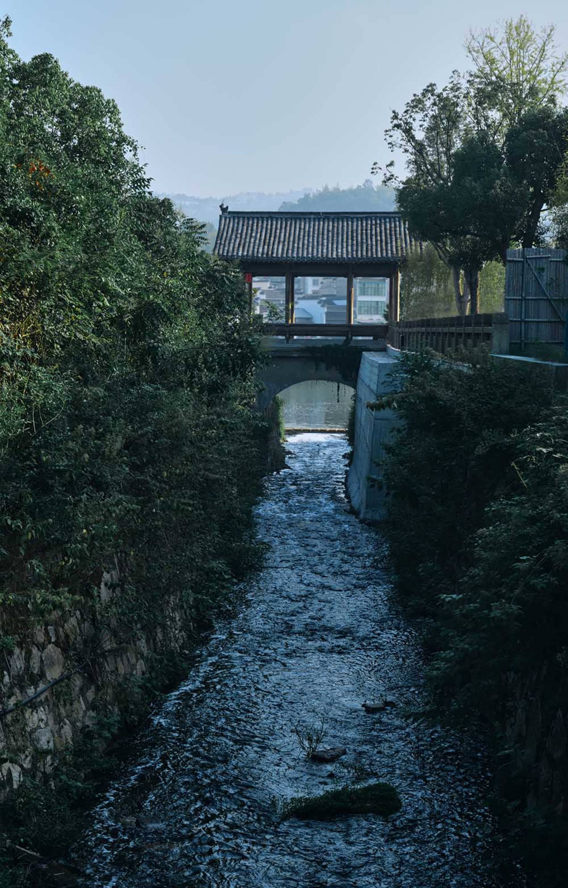 A serene river scene with a stone bridge and a small building nearby, set in a natural environment
