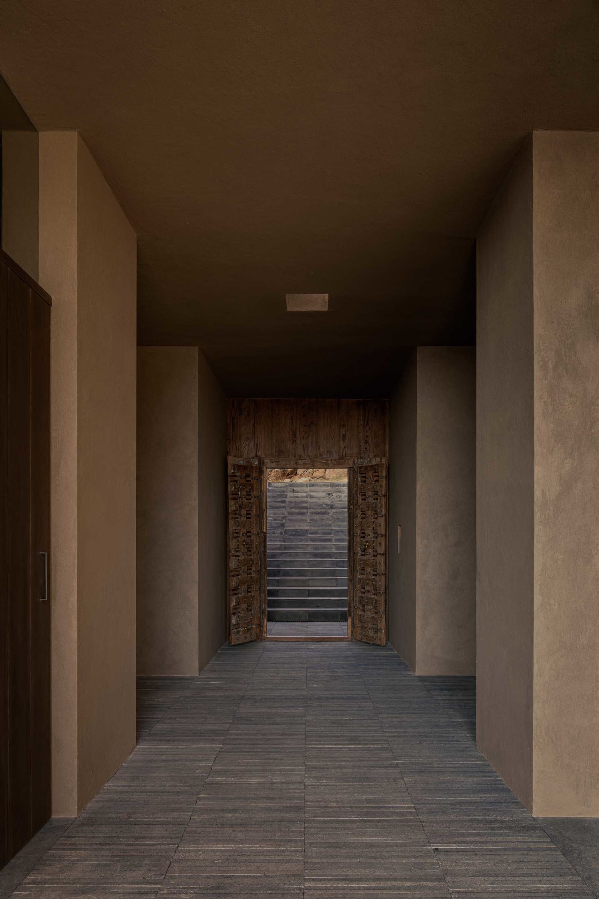 A modern hallway with a doorway, staircase, and ceiling light, featuring concrete and stone materials in a calm and inviting atmosphere