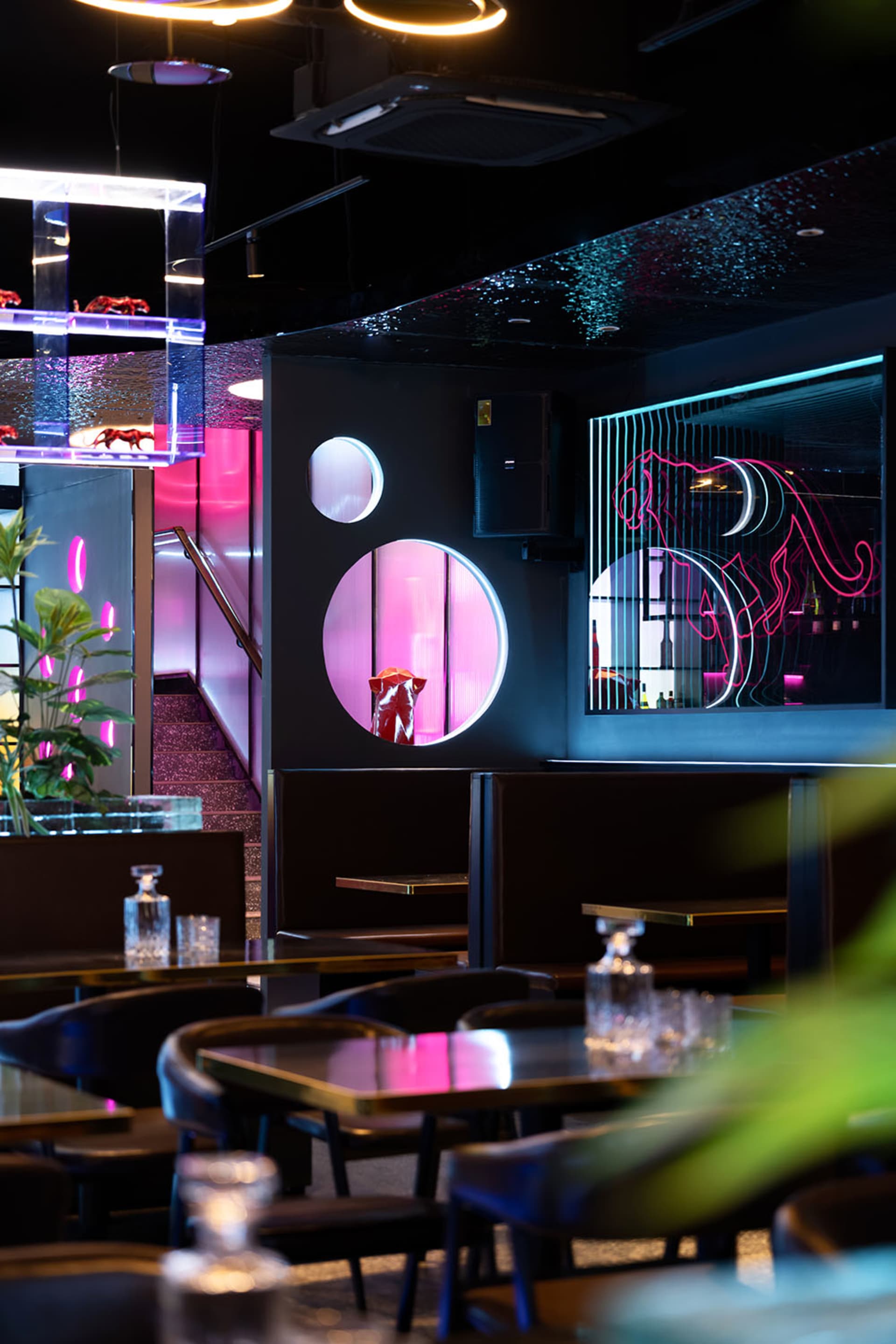 Modern restaurant with black and pink decor, featuring furniture, potted plants, and a stylish atmosphere