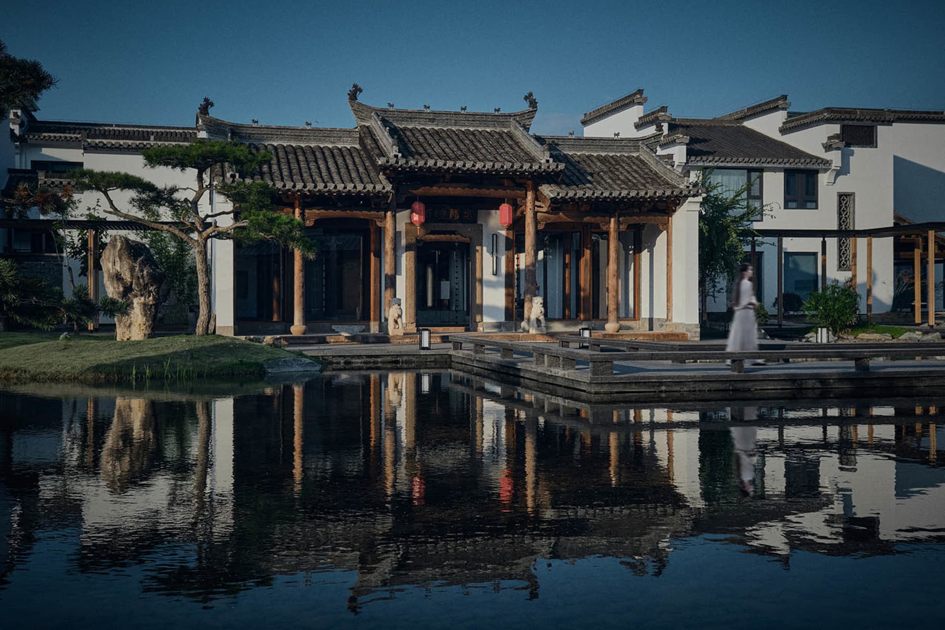 Serene black and white photograph of a Chinese-style building with a pagoda roof, surrounded by a pond and walkway, with statues placed around the area