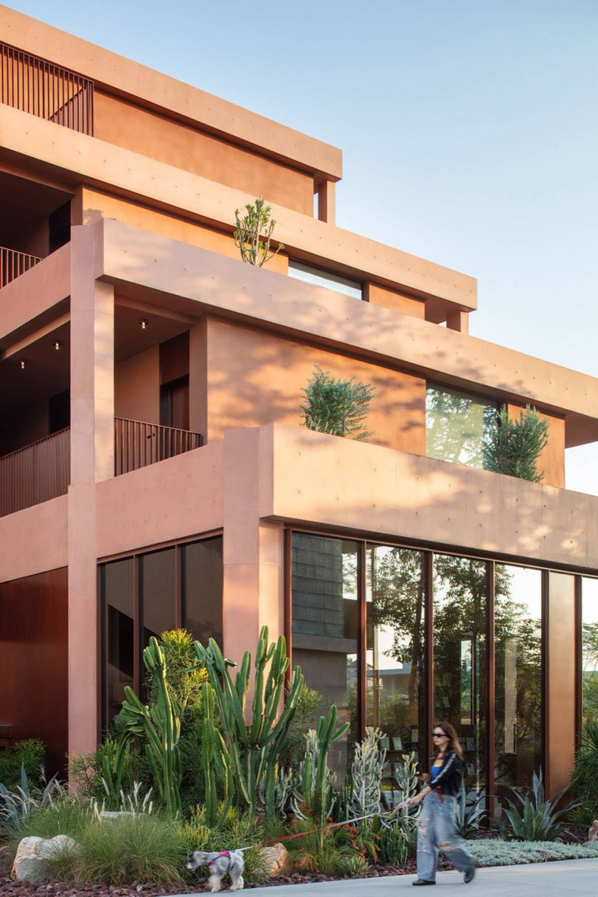 A modern building with a pink and brown color scheme, featuring a large balcony and various windows, with natural light streaming in through the windows