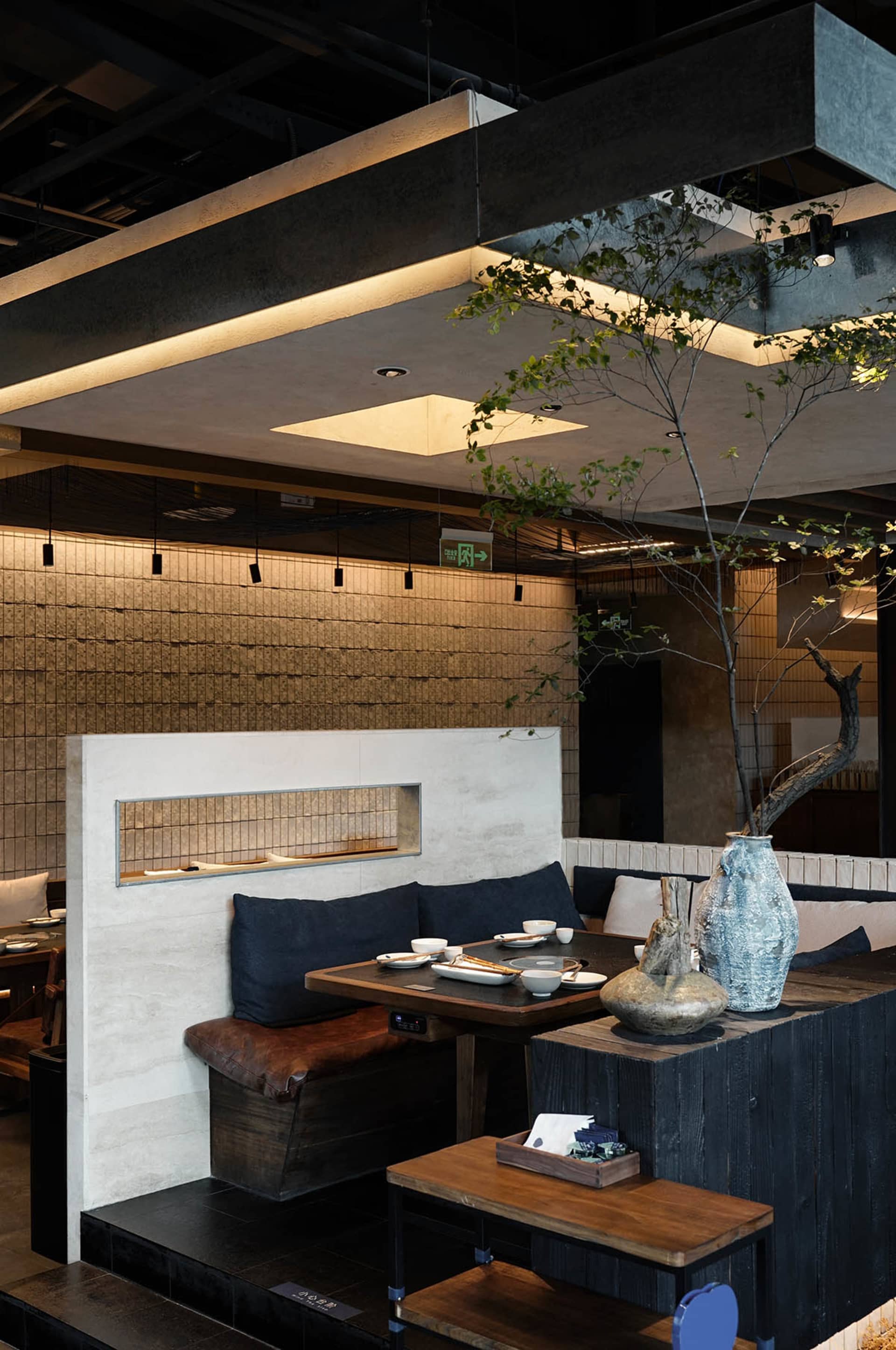 Cozy modern restaurant dining area with a wooden table, chairs, and a potted plant, set with bowls and cups, in a warm and inviting atmosphere