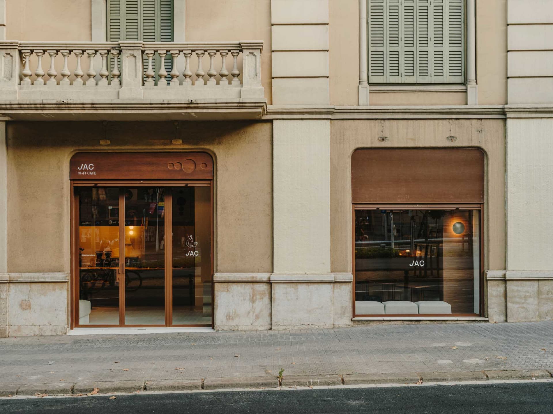 A tan-colored building with a storefront featuring a large brown-framed window, set on a street with a nearby bench, evoking a typical urban atmosphere