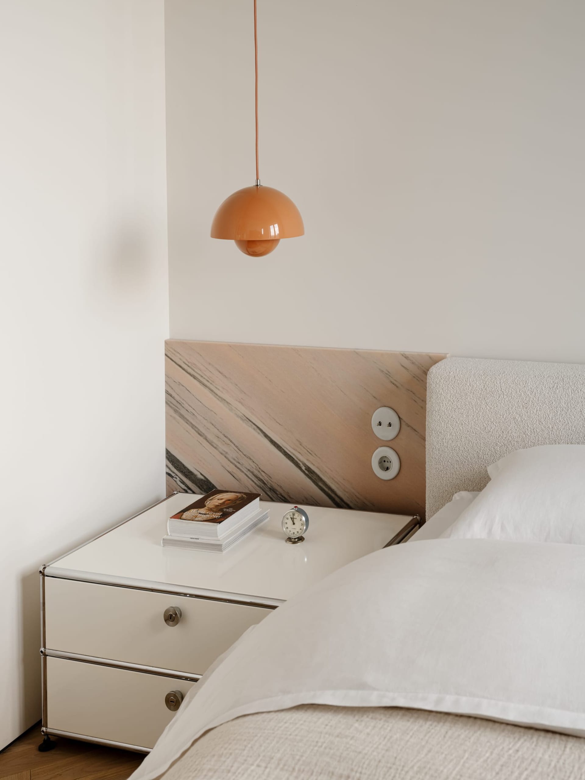 A modern bedroom with a marble-like wall, a bed, nightstand, and lamp, with a clean and luxurious appearance