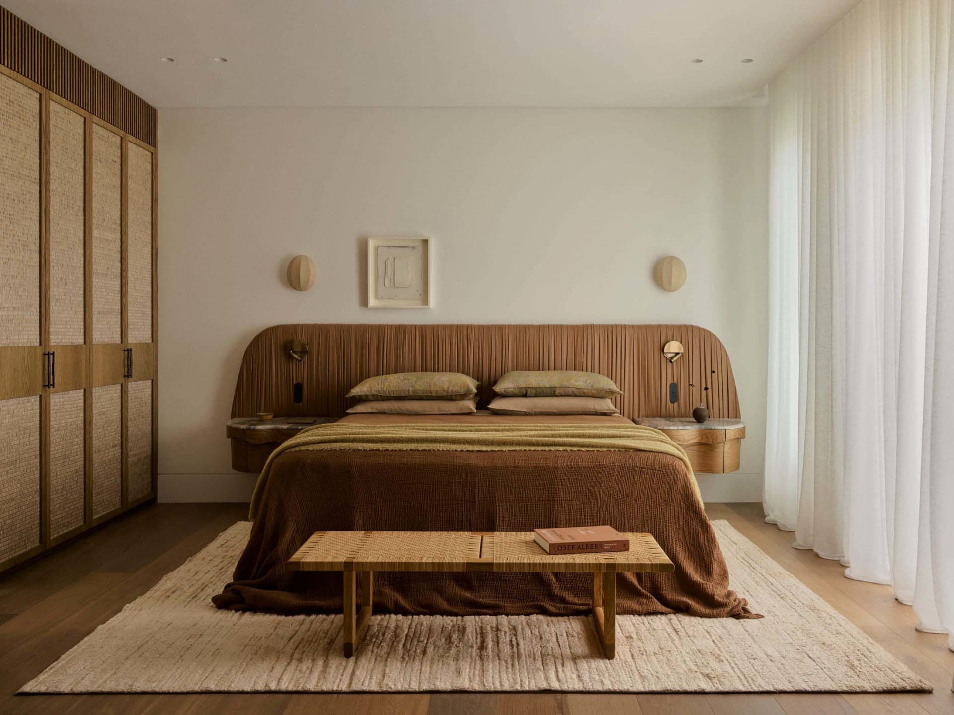 Cozy bedroom with a brown bed, wooden nightstand, and a rug on a wooden floor, against a white wall