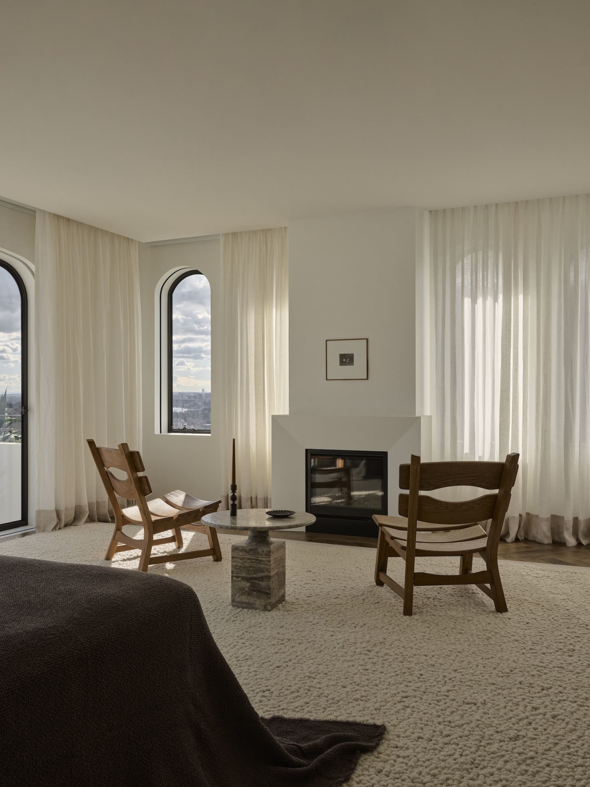Cozy living room with a fireplace, wooden furniture, and a rug, surrounded by natural light from the windows