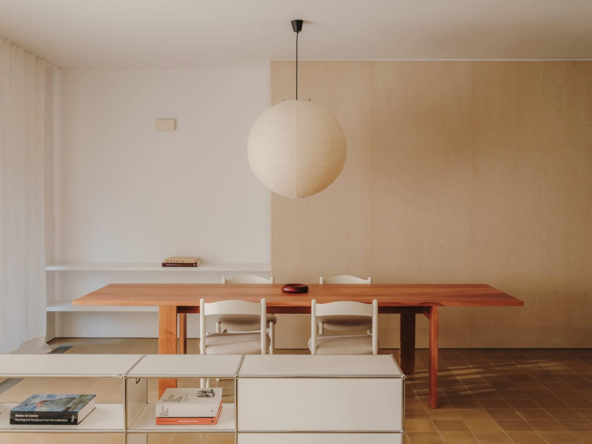 A warm and inviting living room with a wooden dining table, chairs, couch, and bookshelf, lit by natural sunlight