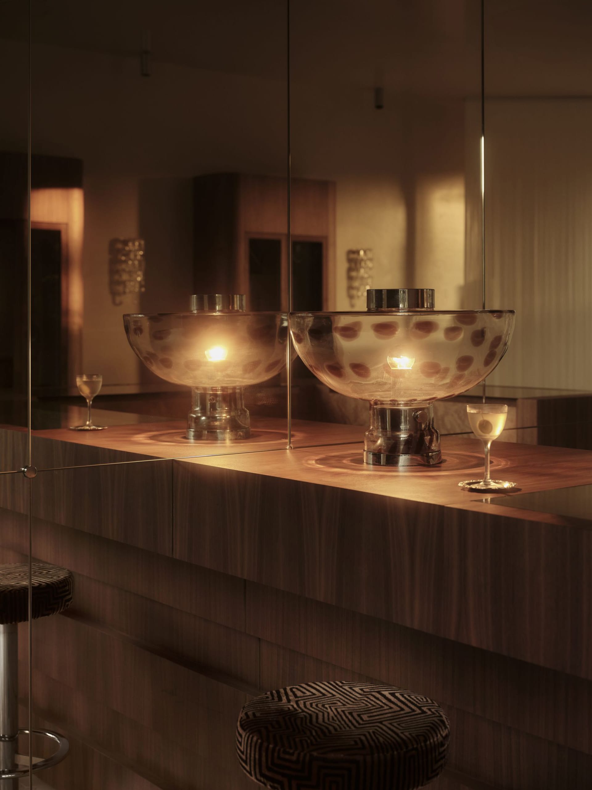 A well-lit bar area with wooden countertops, glass barrier, and decorative vases and wine glasses