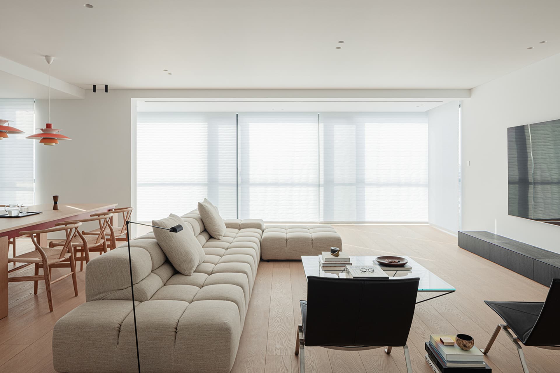 A well-lit modern living room with a white couch, a black chair, a dining table, and a TV, creating a bright and inviting atmosphere