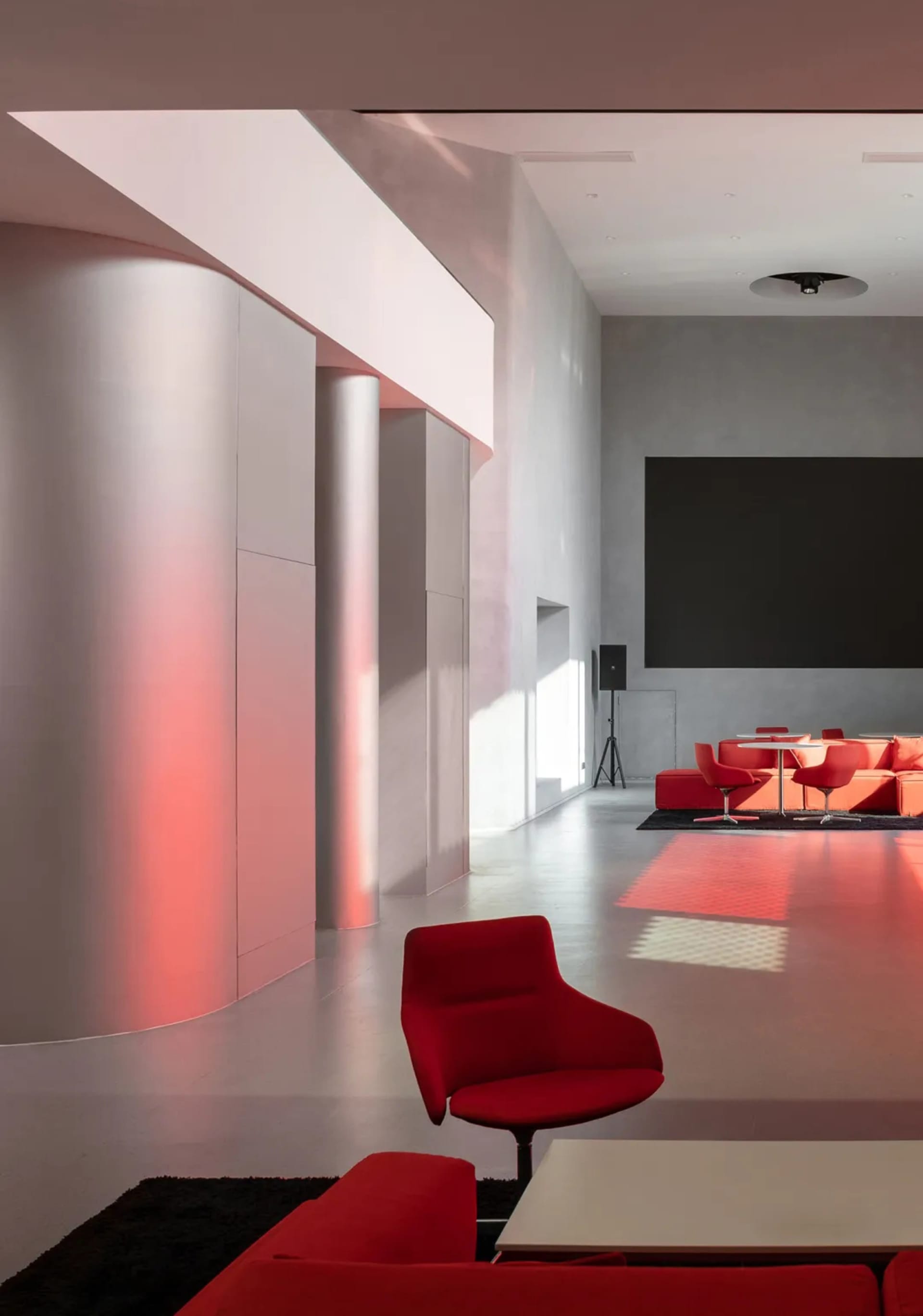 A well-lit lobby with a red chair, ottoman, and dining table, featuring a large screen and comfortable seating