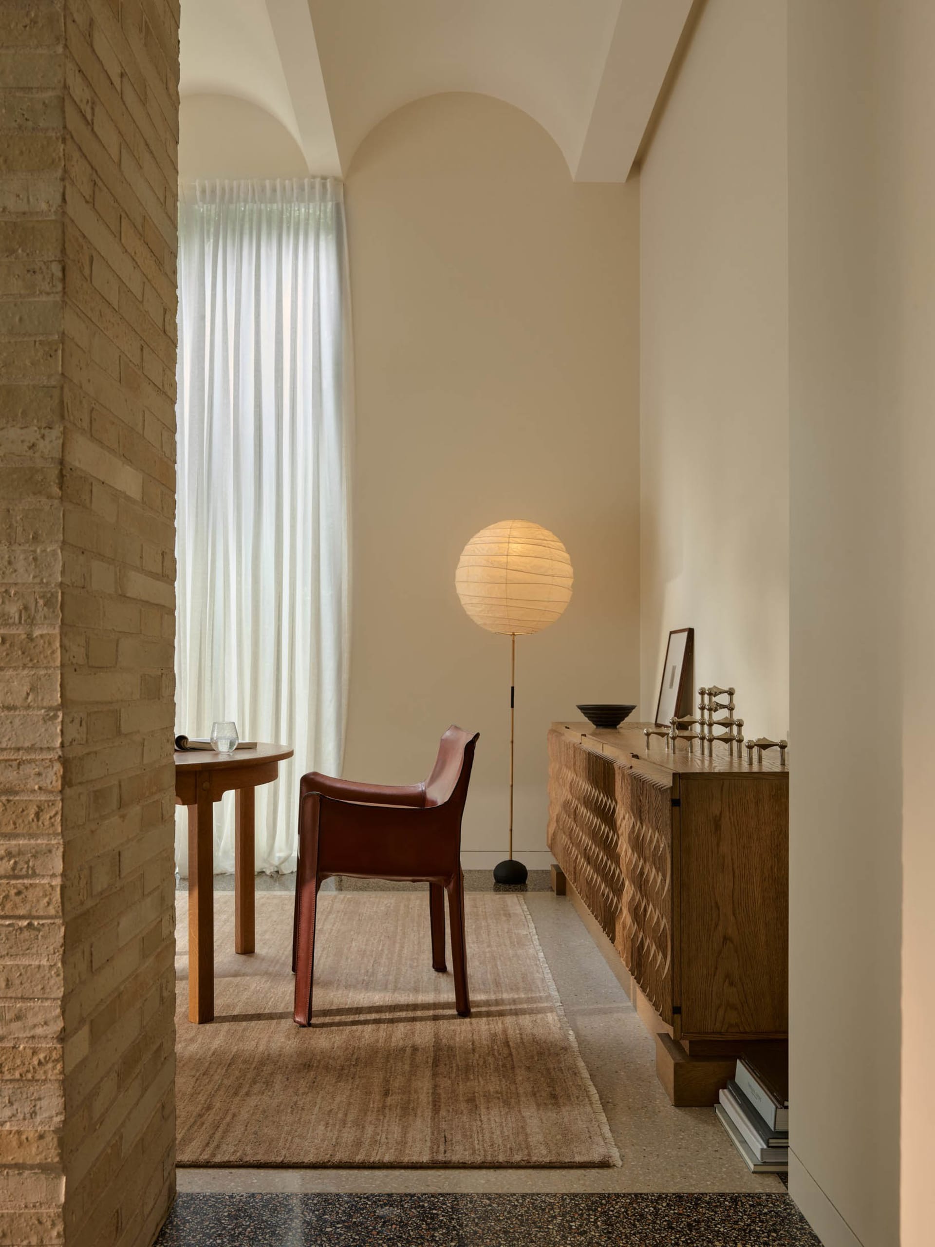 Cozy living room with a brick wall, hardwood floor, a red chair, a table, and a lamp, well-lit and inviting