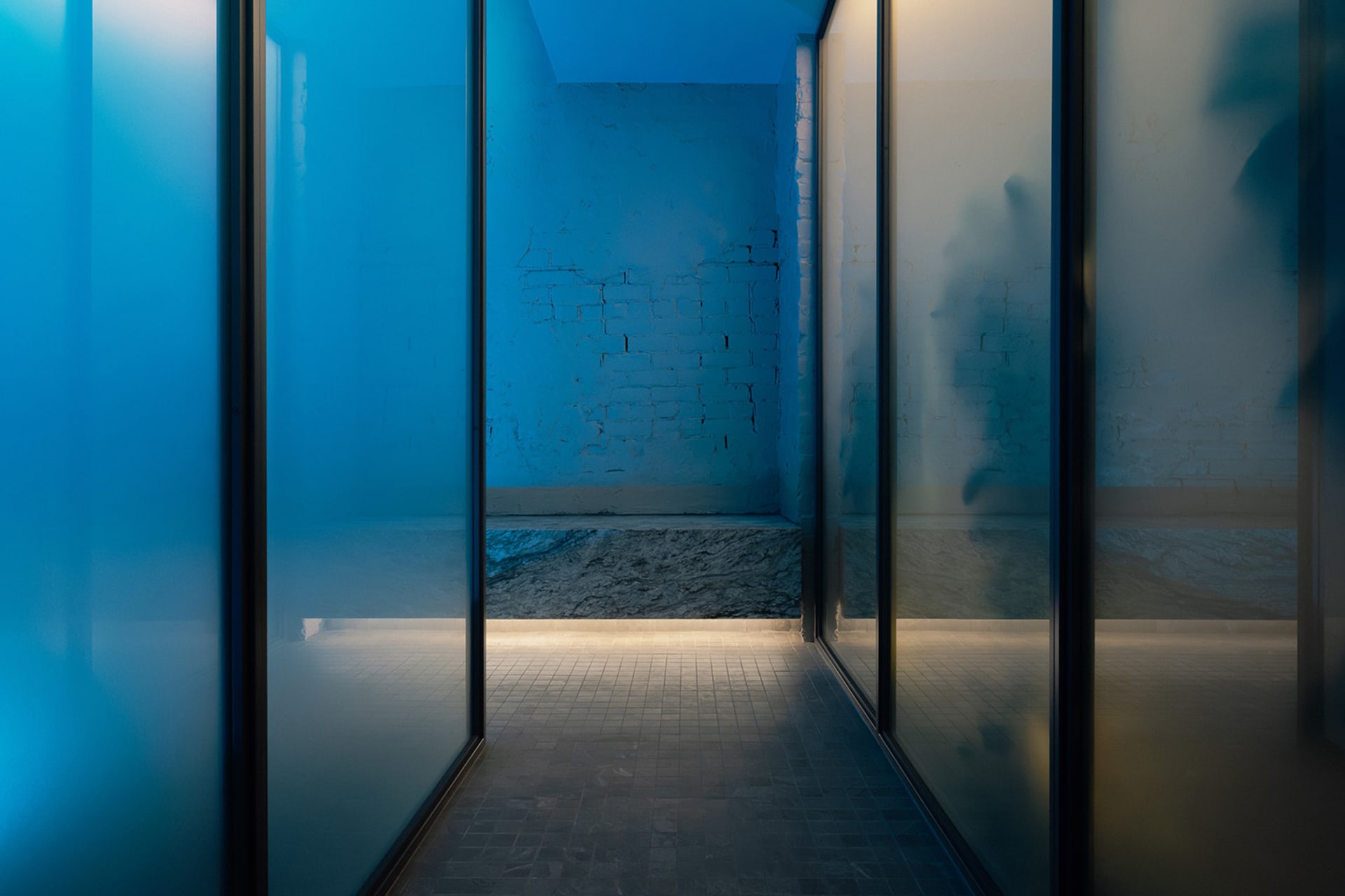 Dimly lit hallway with brick walls, glass doors, and natural light from windows