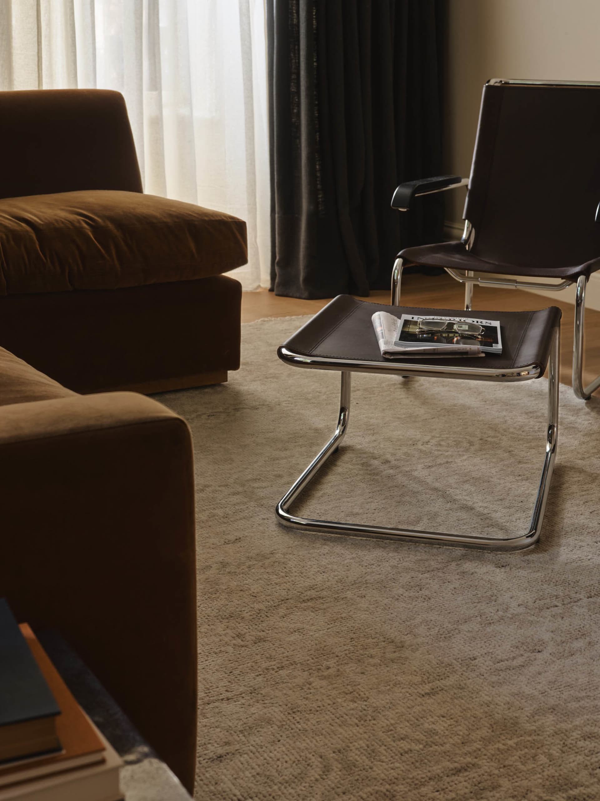 A modern living room with a brown couch, chair, and coffee table, set against a carpeted floor with a magazine on the coffee table
